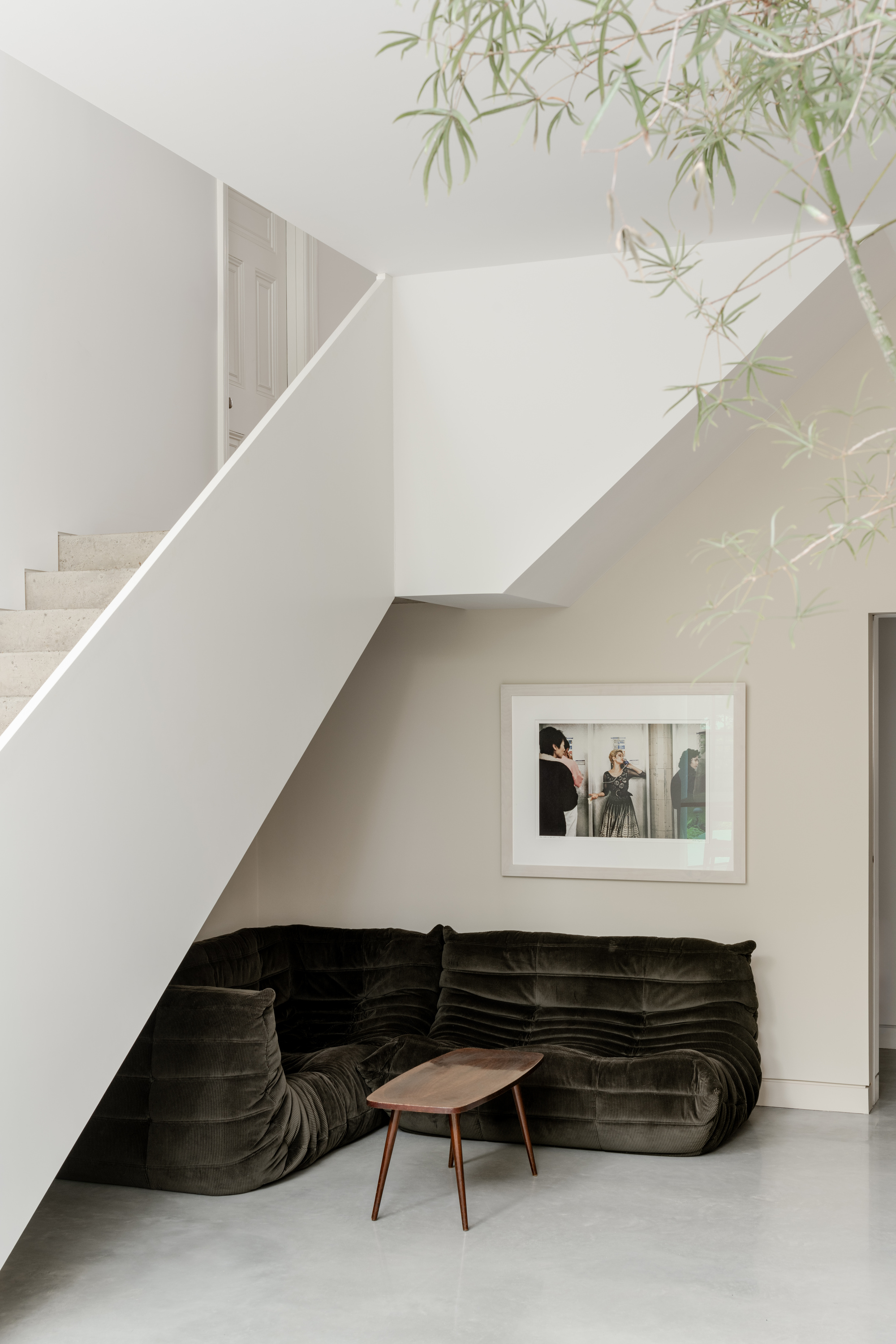 Seating nook beneath the staircase with dark velvet sofa and overhanging bamboo branches