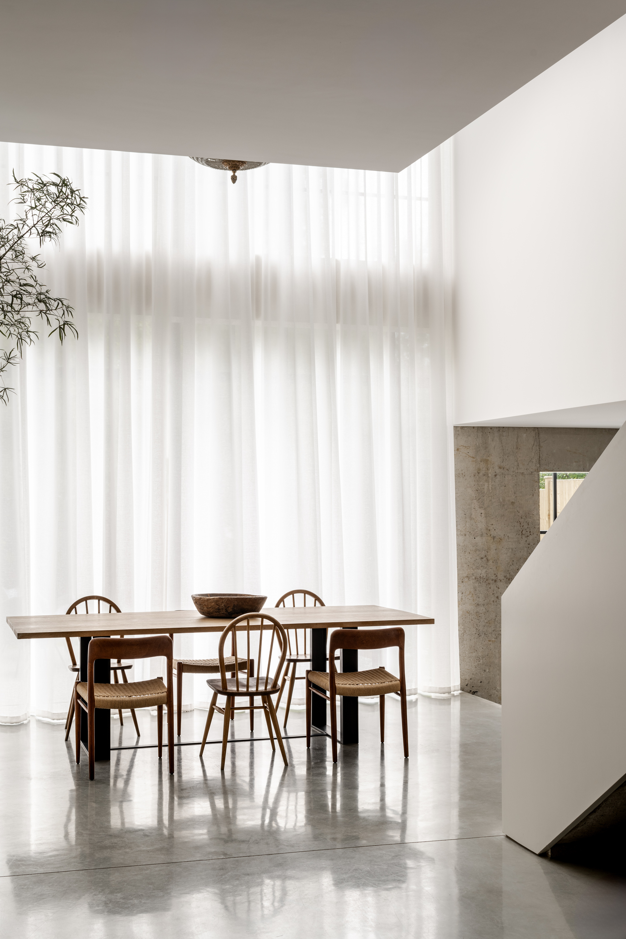 Dining area with timber table and cane chairs beneath a white translucent curtain wall with diffused light