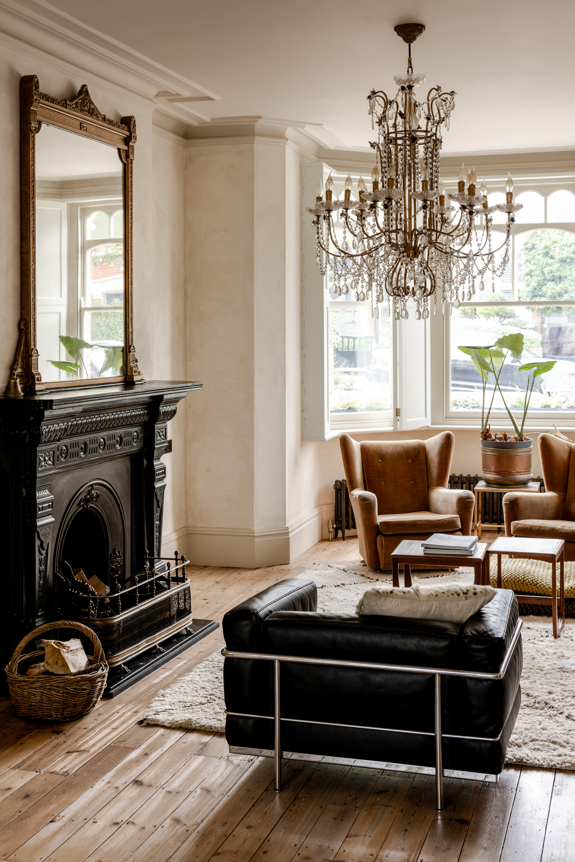 Living room with ornate black fireplace surround and crystal chandelier above leather and tan upholstered seating