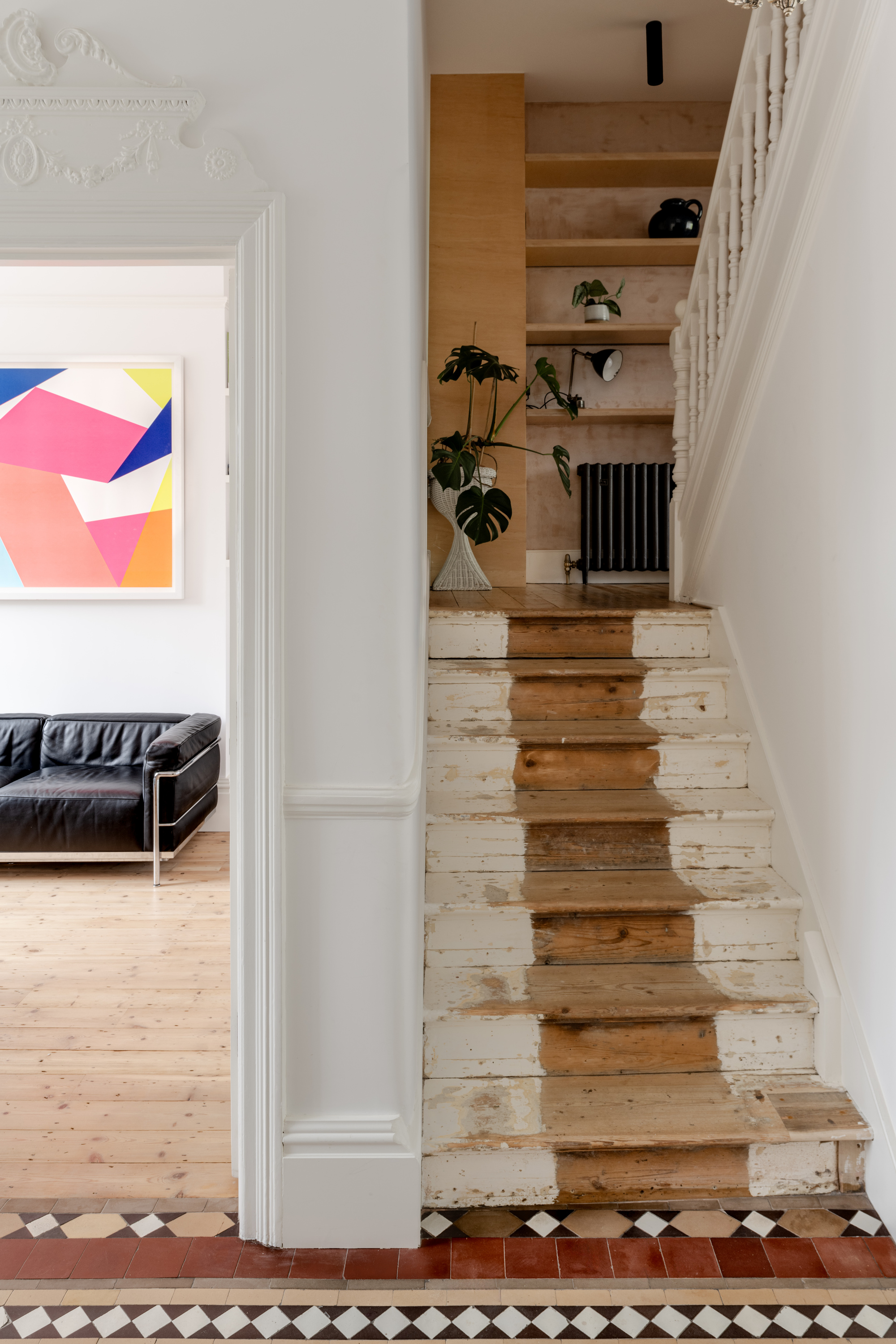 Timber and white painted staircase rising toward built-in shelving with potted monstera plants