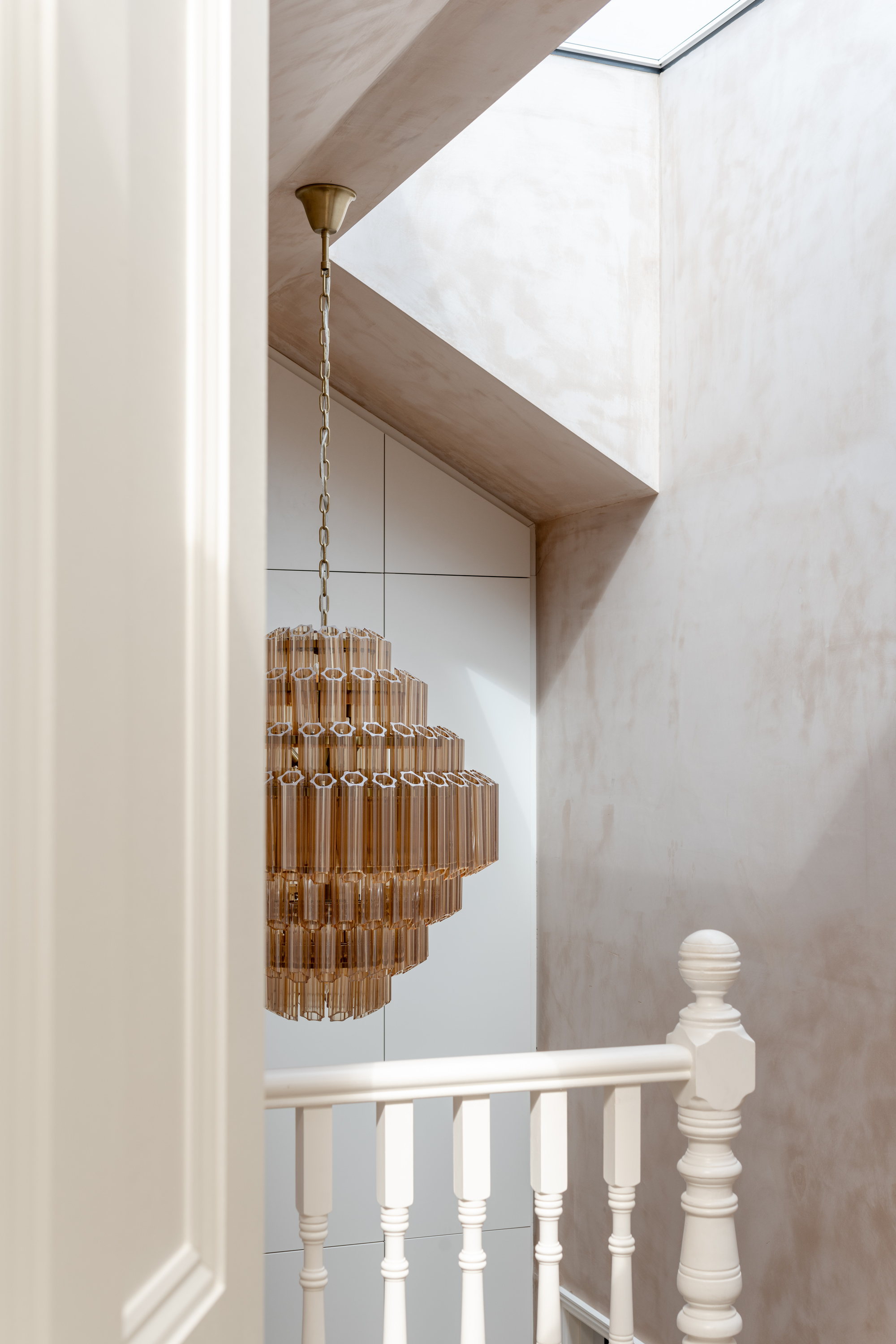 Tiered brass and glass chandelier hanging in double-height stairwell with skylight above white balustrade