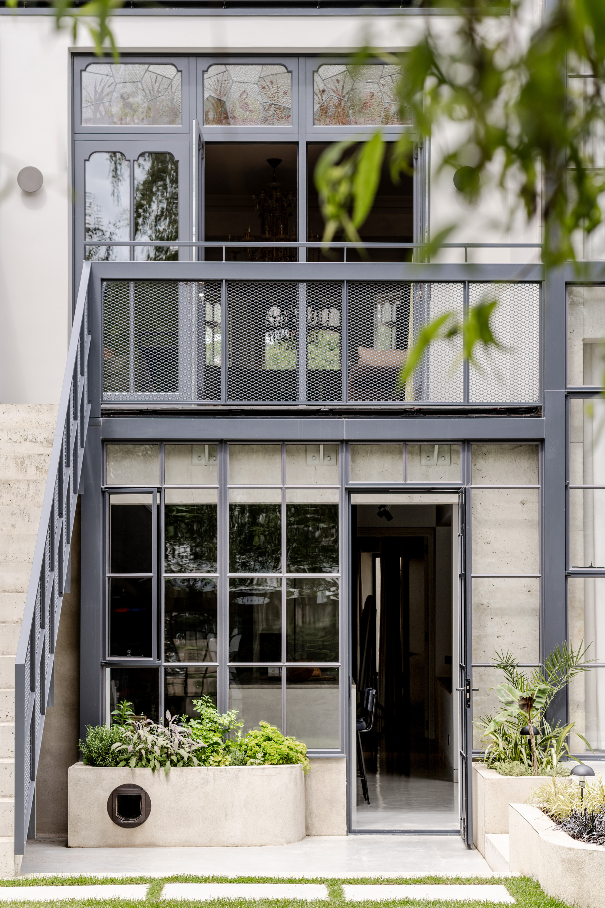 Ground level facade detail with decorative glass transoms, expanded metal balcony and planted concrete beds