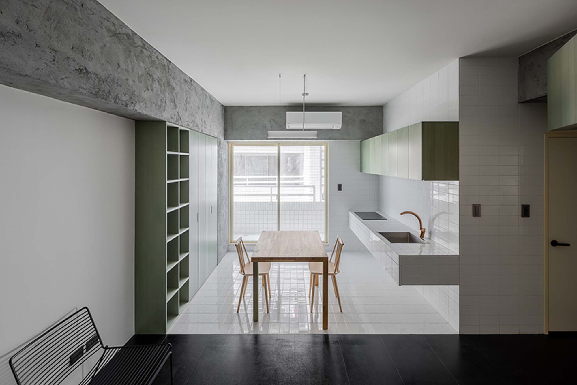 Kitchen and dining area with white tile backsplash, timber table, and pale green storage against concrete walls