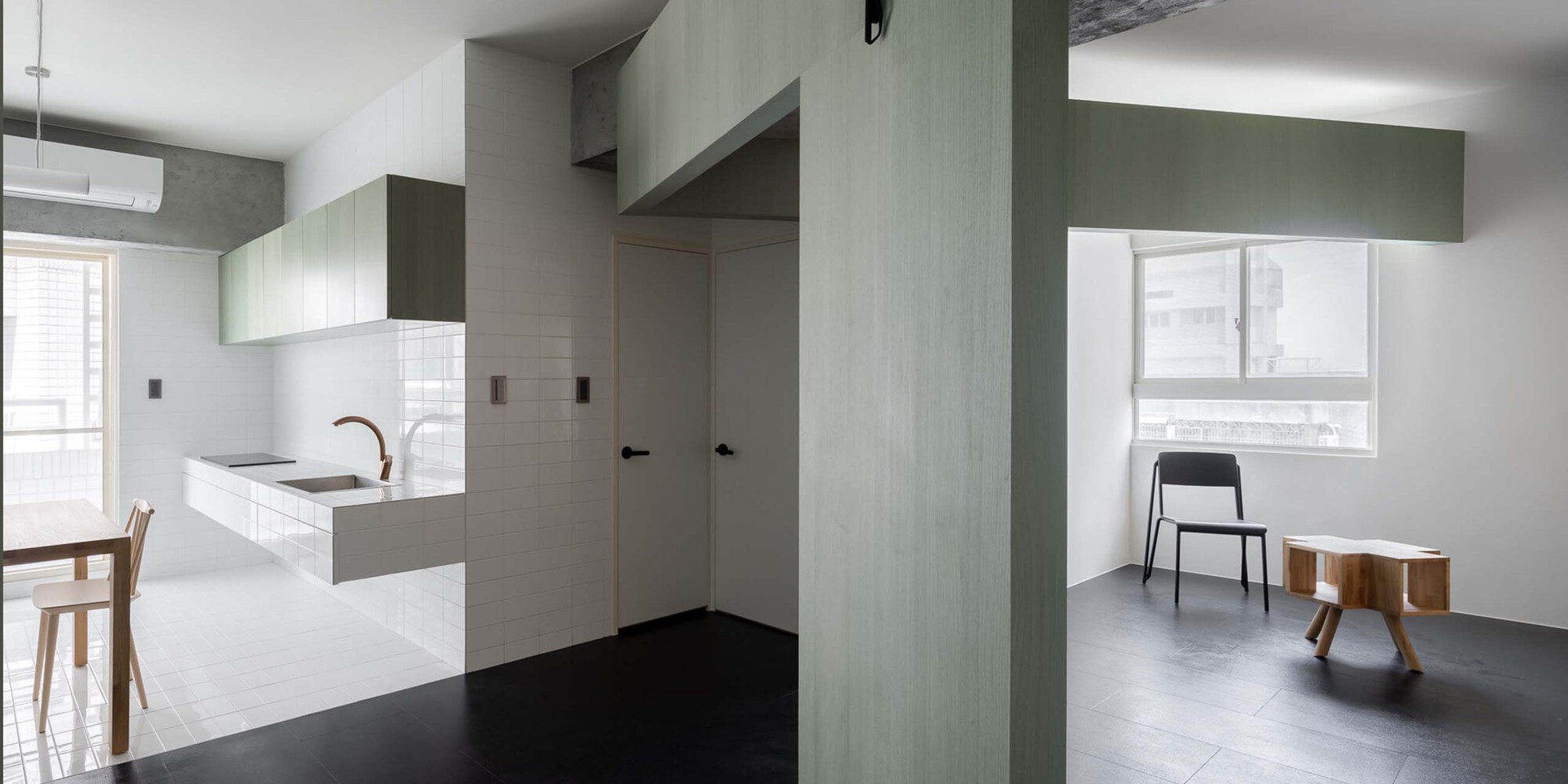View through pale green paneled partition wall dividing the kitchen from the living zone with black flooring