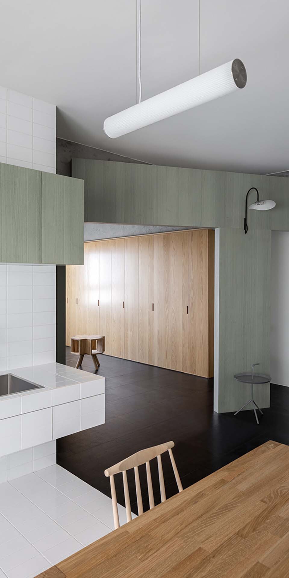 Timber wardrobe wall beneath tubular pendant light with pale green partition and black floor in foreground