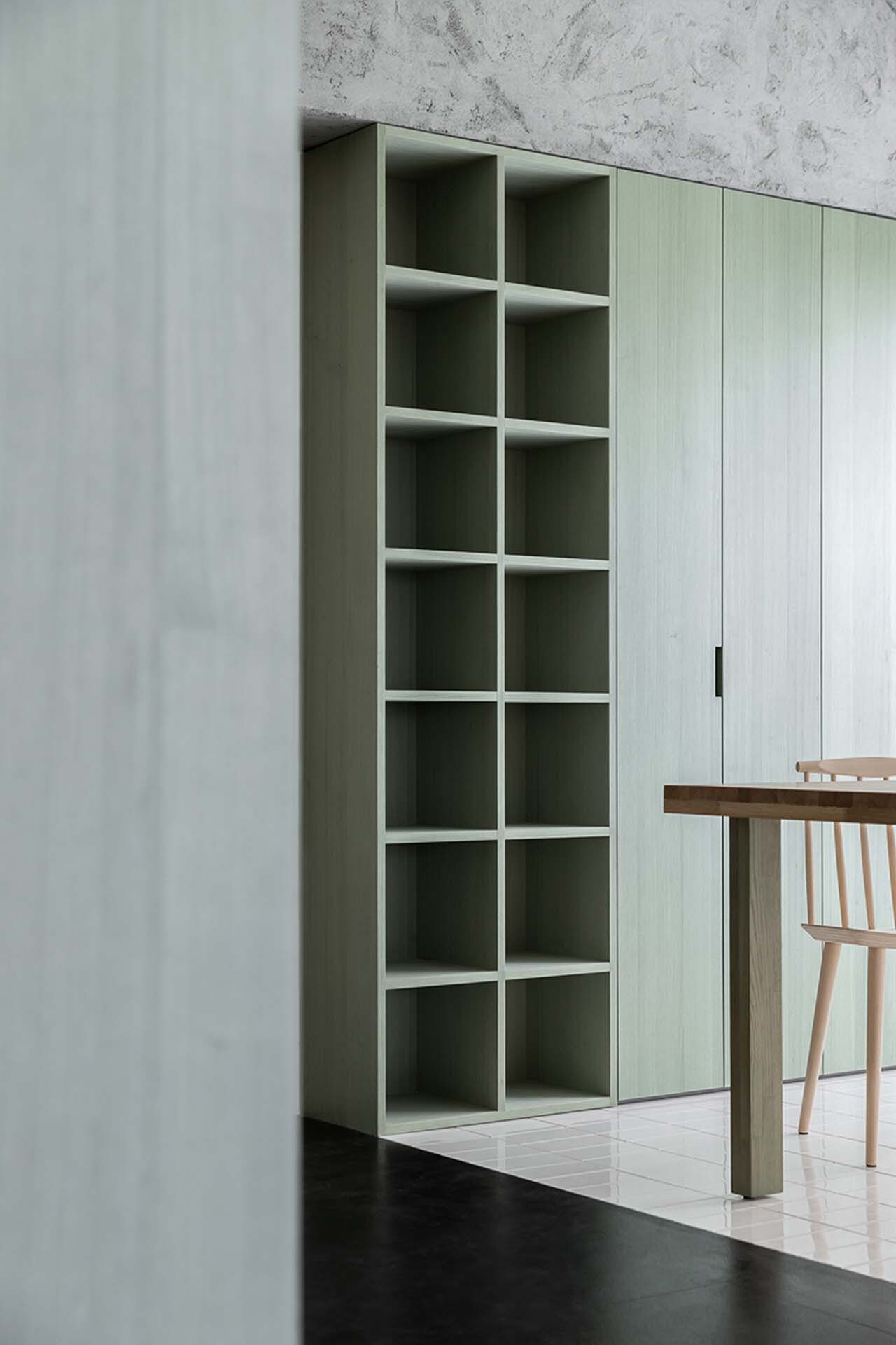 Detail of pale green open shelving unit beside timber dining furniture against exposed concrete wall