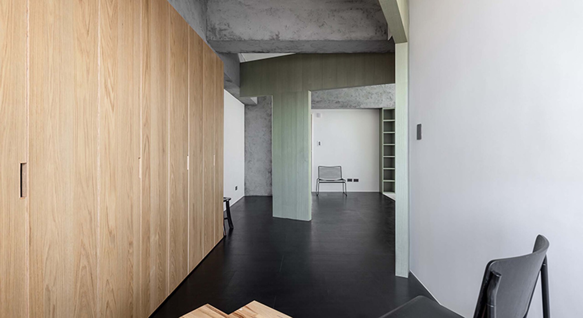 Corridor with timber storage wall and pale green partition framing views through connected interior spaces