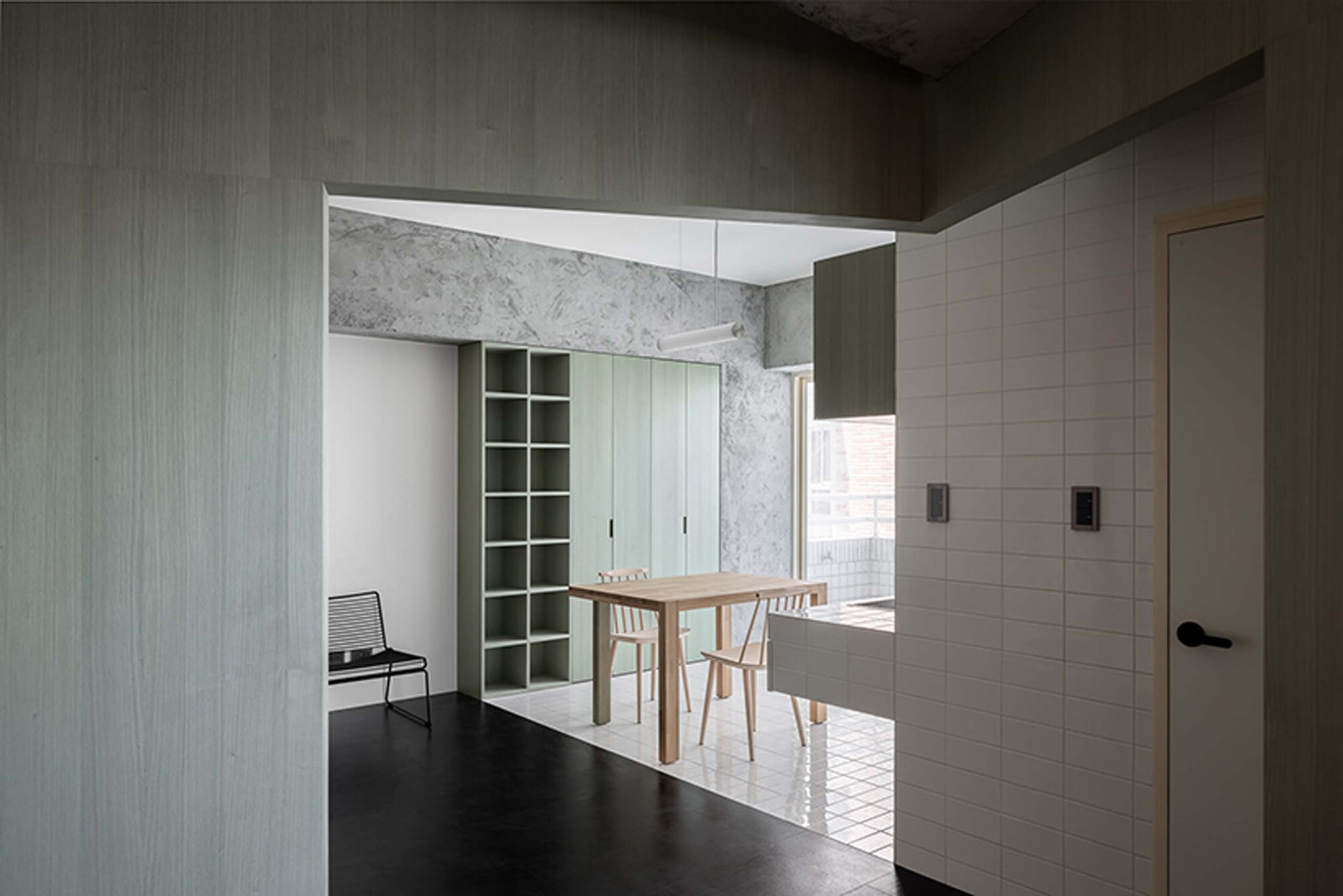 View through doorway into dining area with pale green shelving and marble portal framing