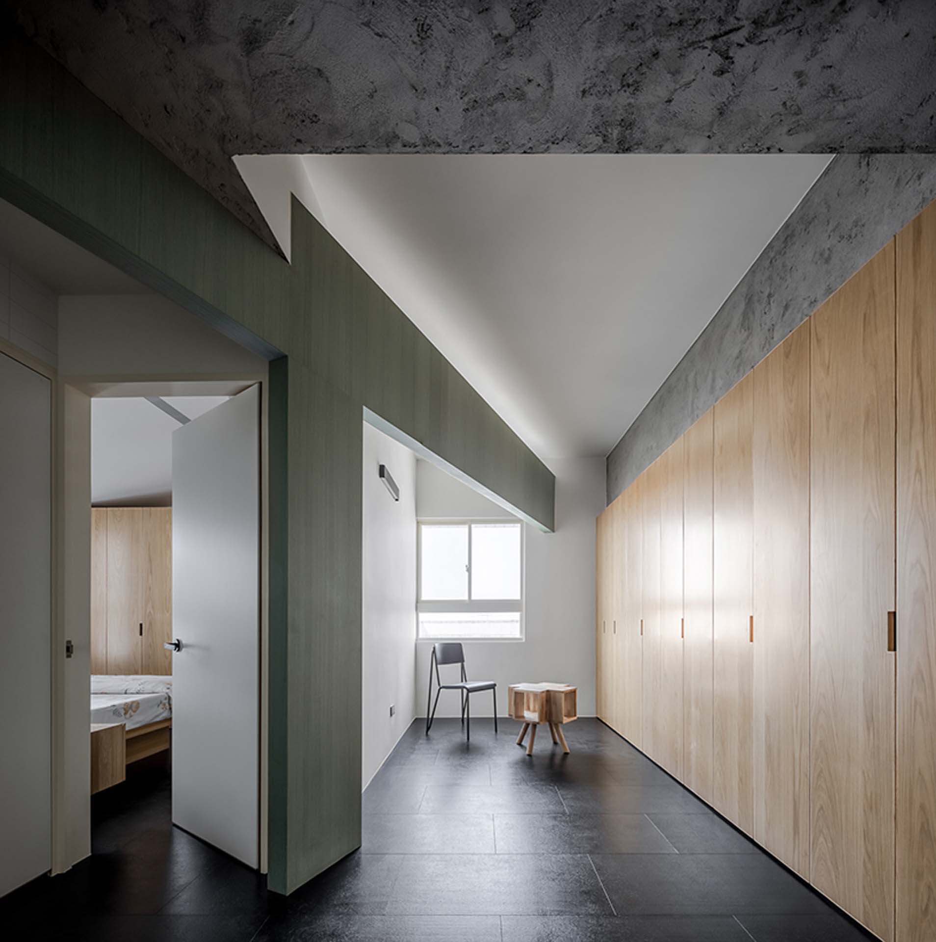 Hallway with triangular white ceiling vault and timber wardrobes along exposed concrete walls