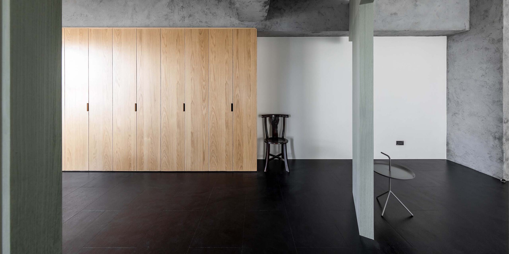 Open room with timber storage wall and exposed concrete ceiling beams in daylight