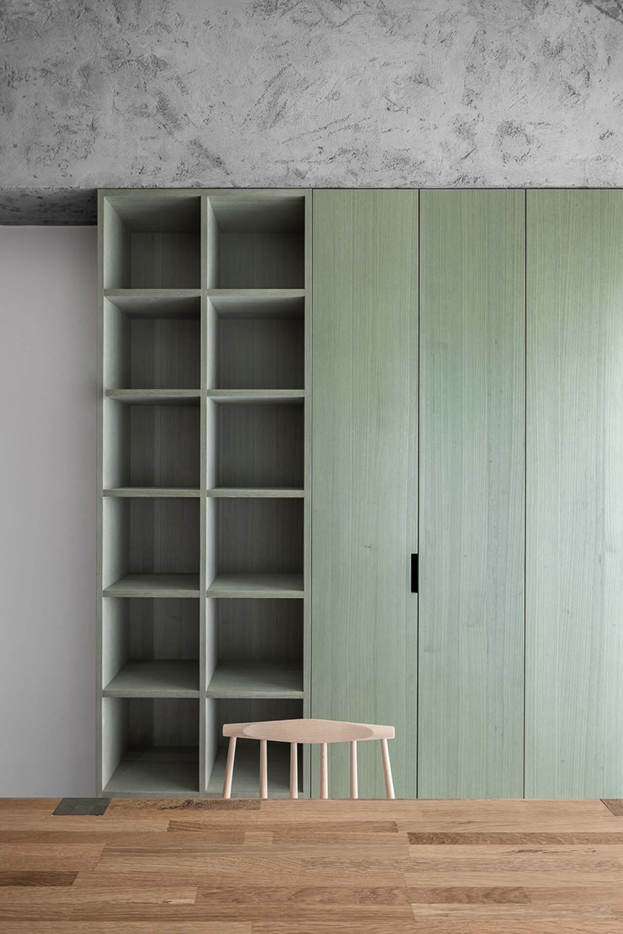 Storage wall with pale green cabinetry and open grid shelving against concrete ceiling