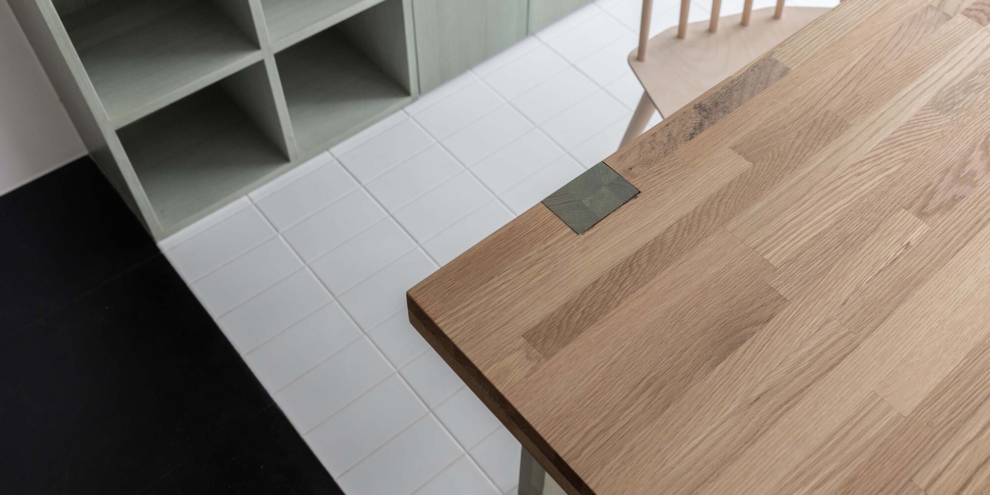 Detail of timber table edge meeting white tile floor and black resin flooring