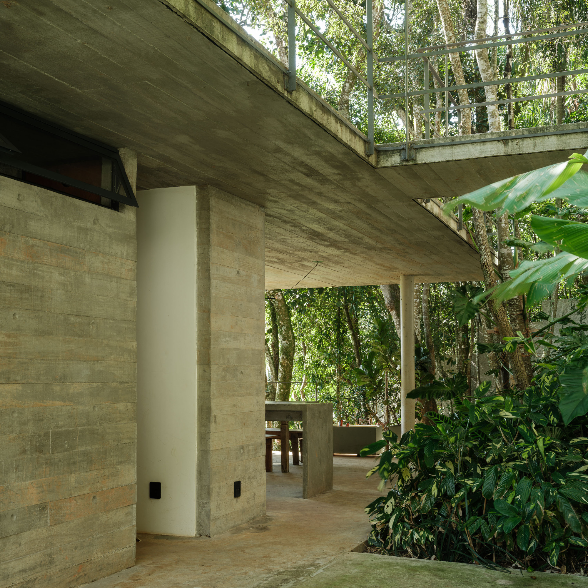 Staggered concrete terraces with exposed formwork connected by columns and surrounded by dense forest vegetation