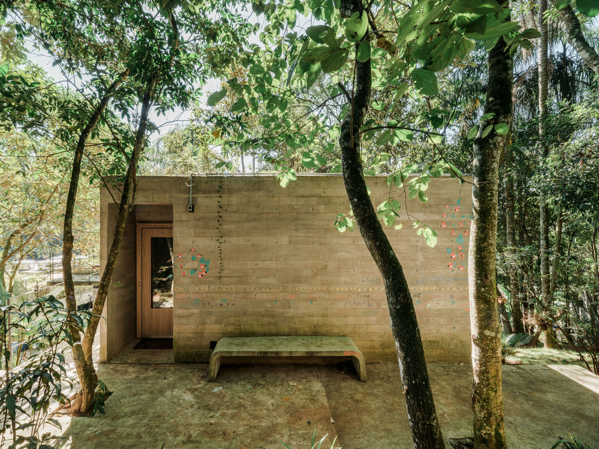 Board-formed concrete wall with timber door and bench beneath overhanging tree branches