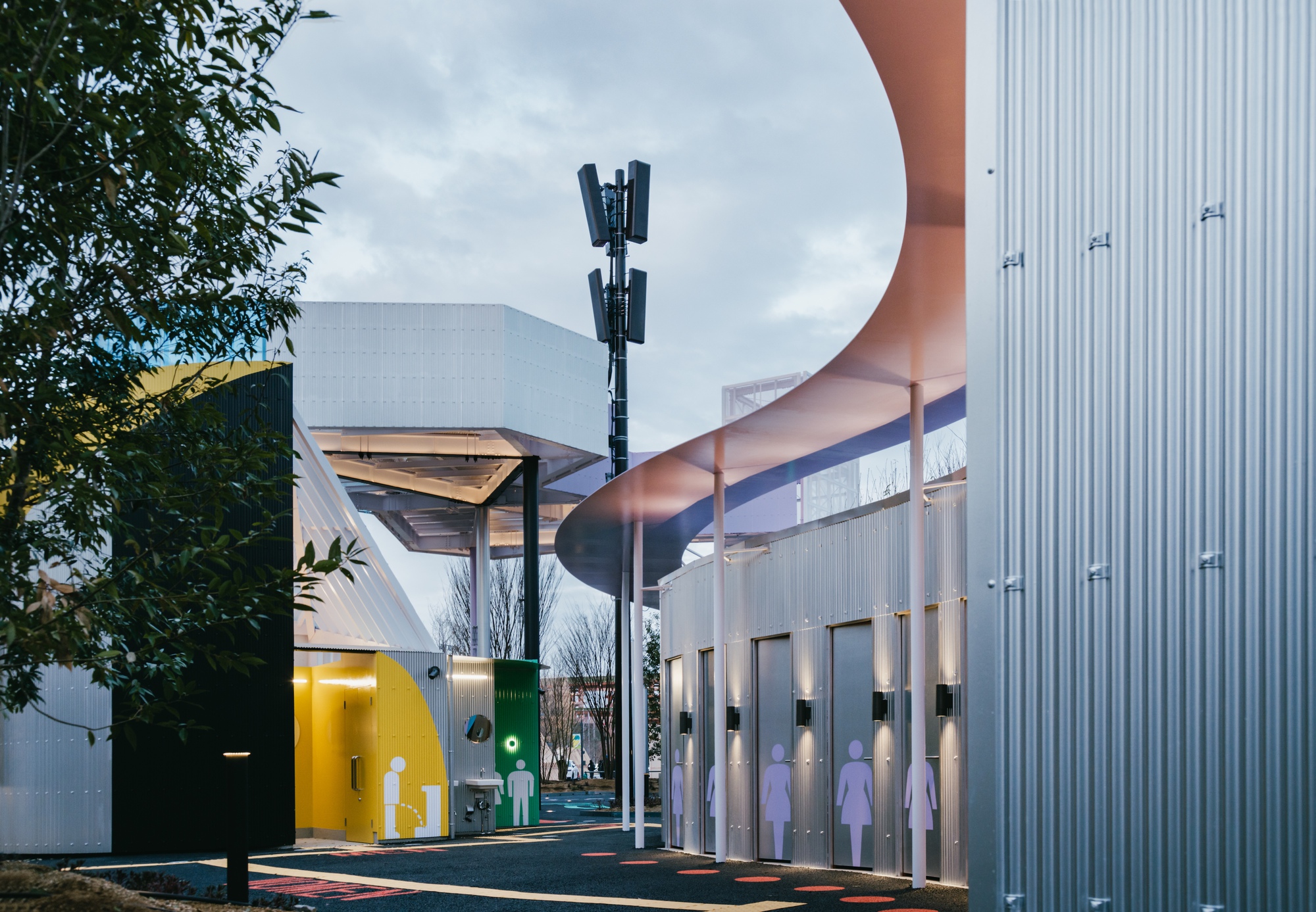 Curved tubular signage element above a corrugated metal wall with silhouette graphics at twilight