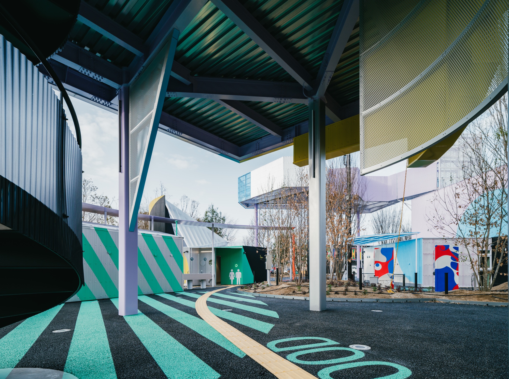 Sheltered walkway with angled corrugated roof panels and green-striped paving below bare winter trees