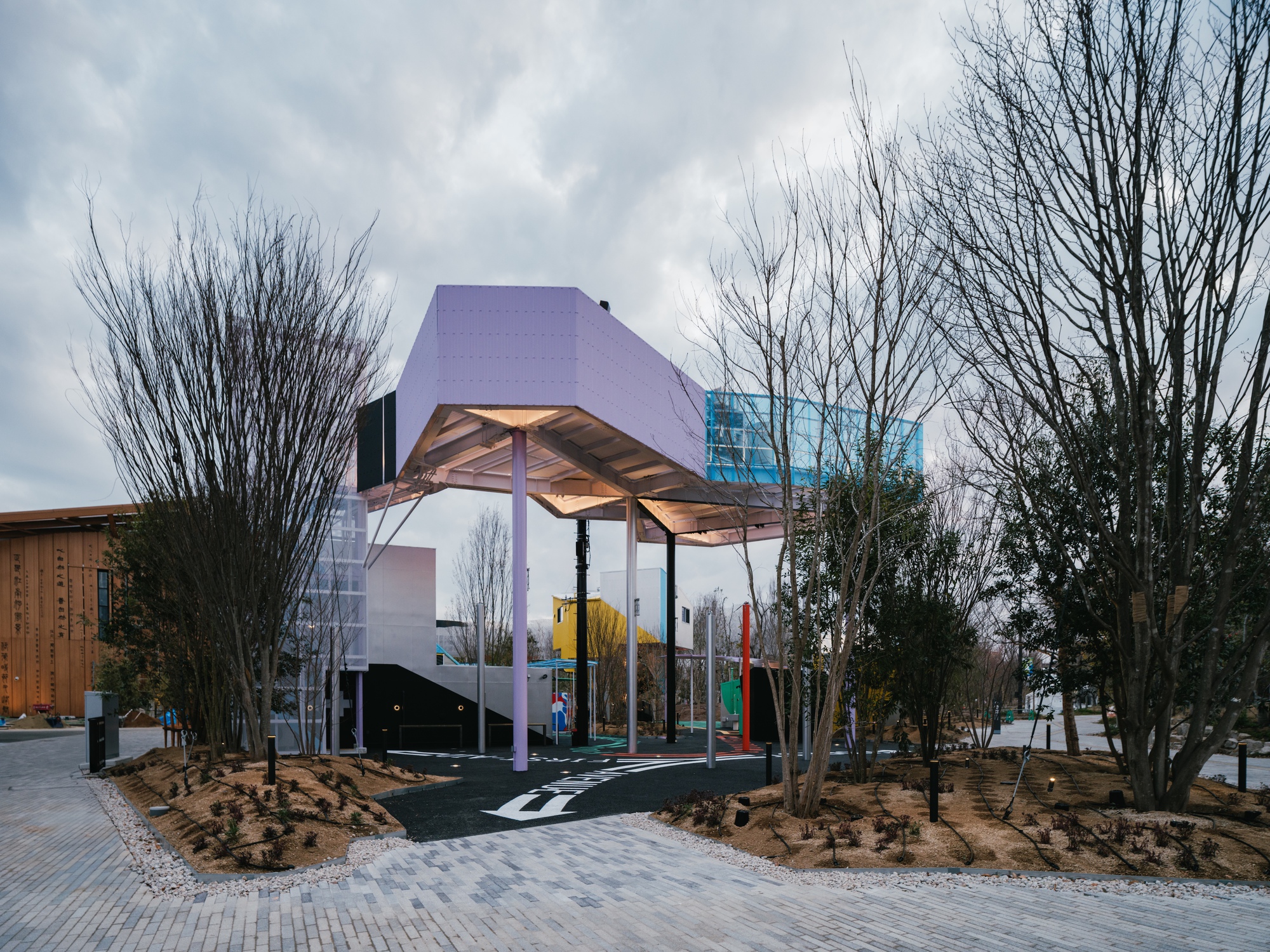 Canopy pavilion with exposed timber rafters among bare trees under an overcast sky