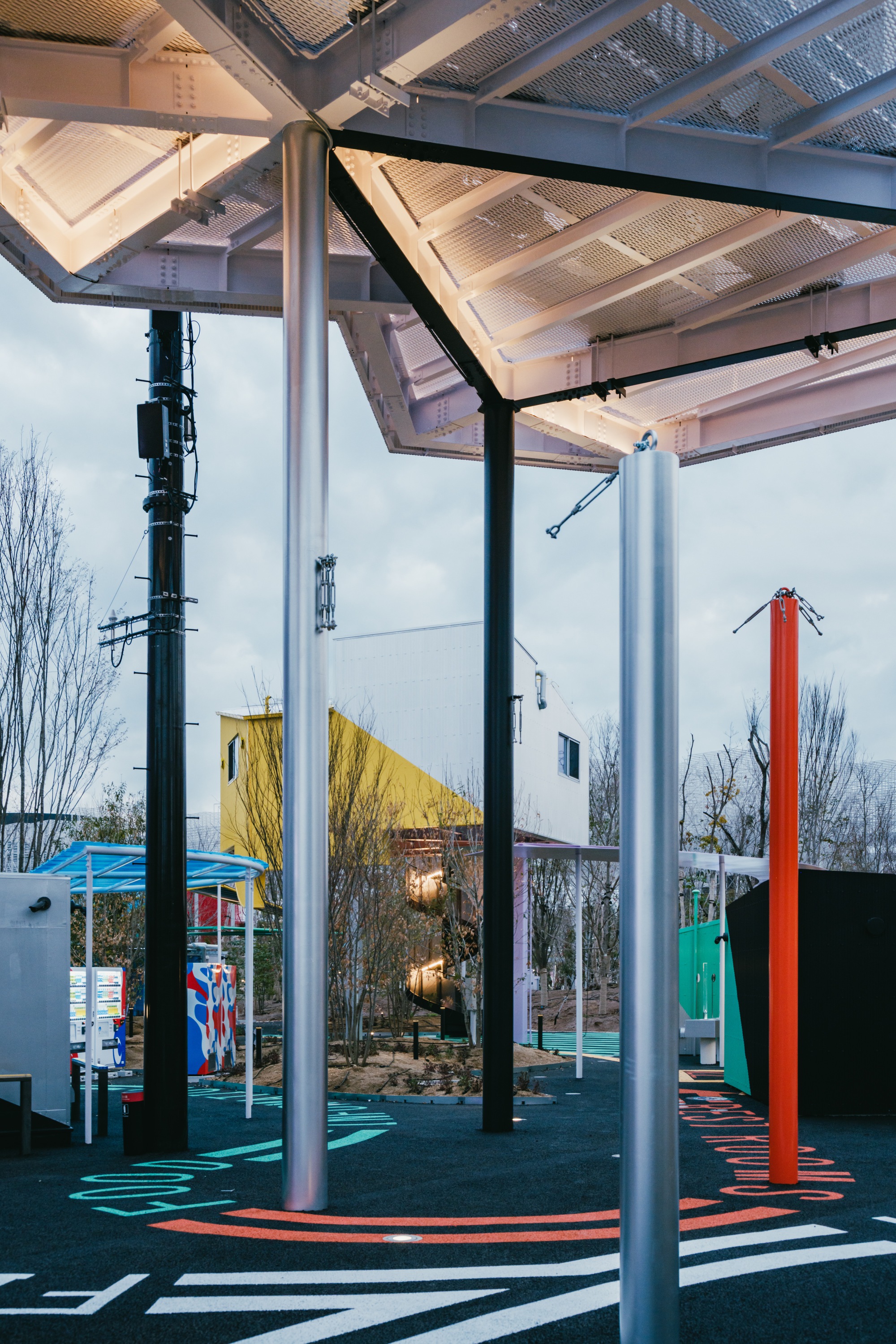 Steel column detail with perforated metal canopy panels and view to neighboring corrugated buildings under overcast sky