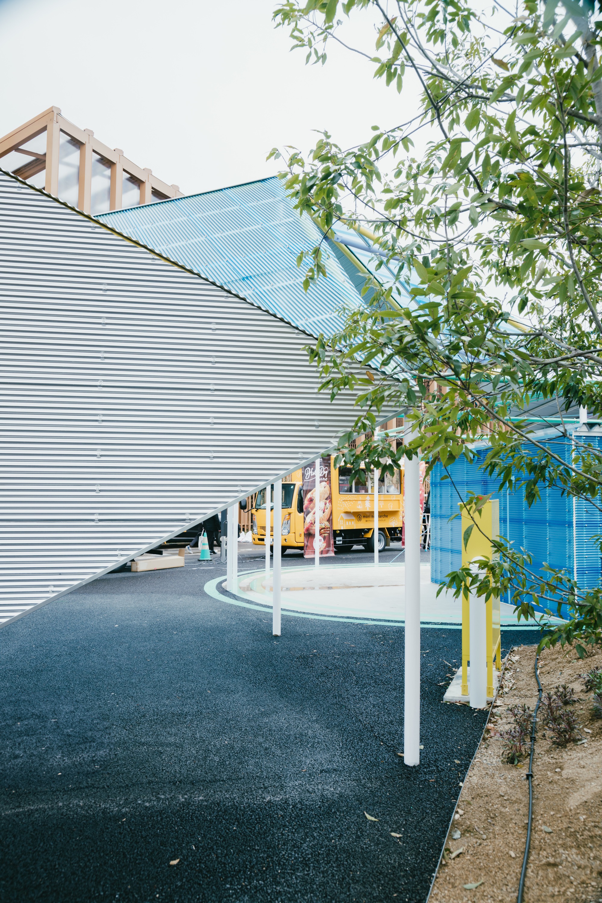 Corrugated metal curved wall with white columns and young tree branches in foreground under soft daylight