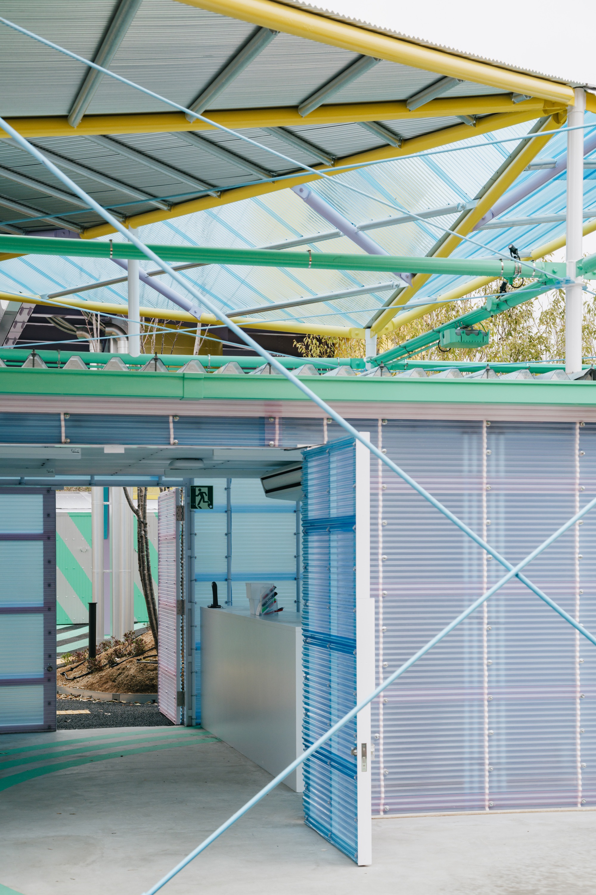 Entry to a corrugated metal pavilion with exposed steel structure and translucent polycarbonate wall panels