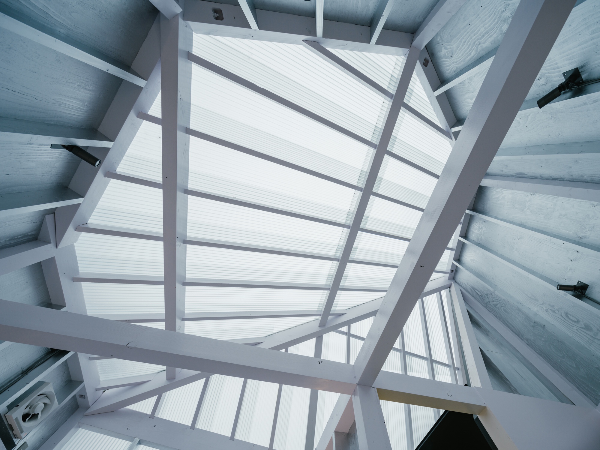 Upward view through the translucent corrugated roof framed by white steel beams and concrete walls