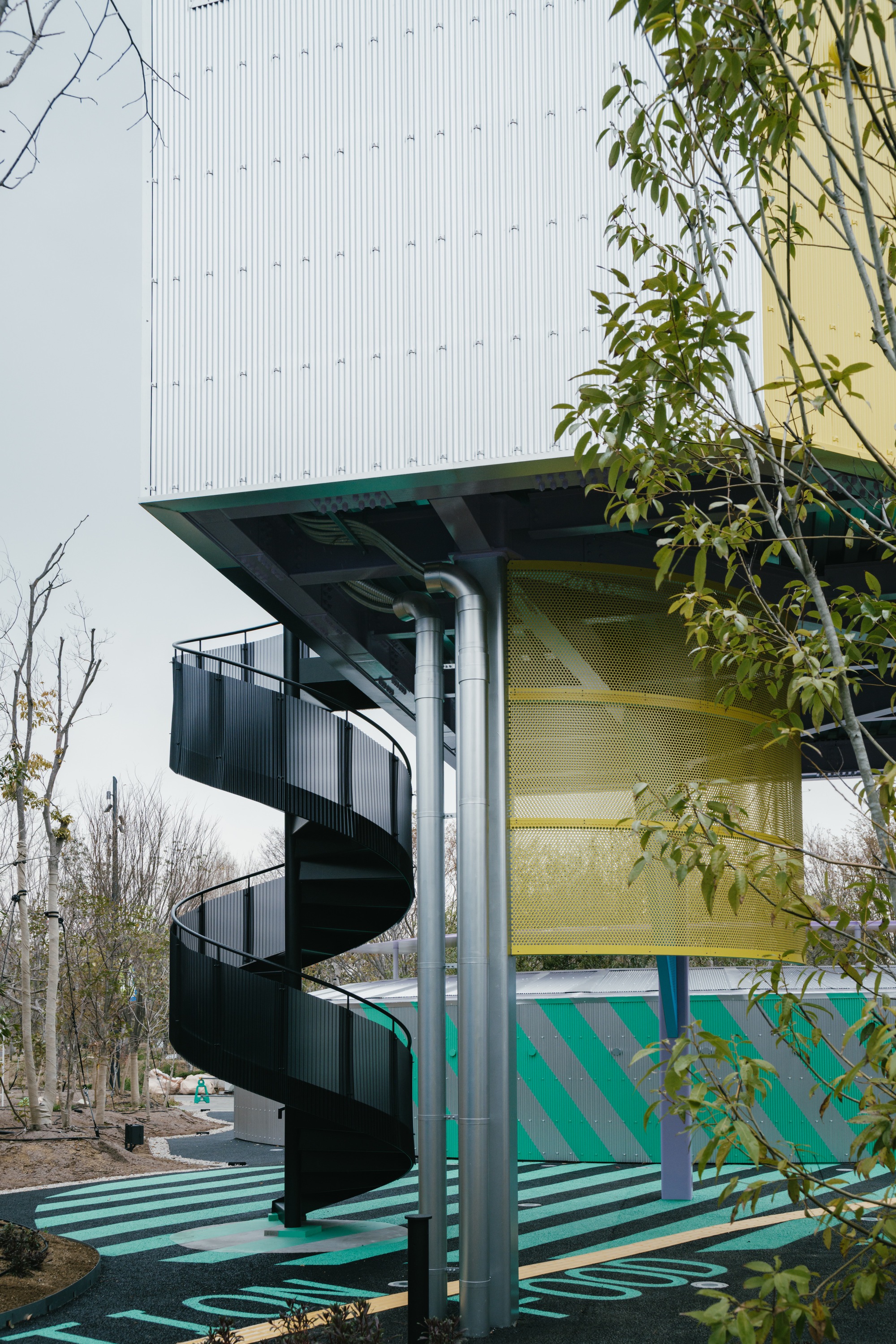 Black spiral staircase beneath a cantilevered volume with yellow panel and striped ground pattern