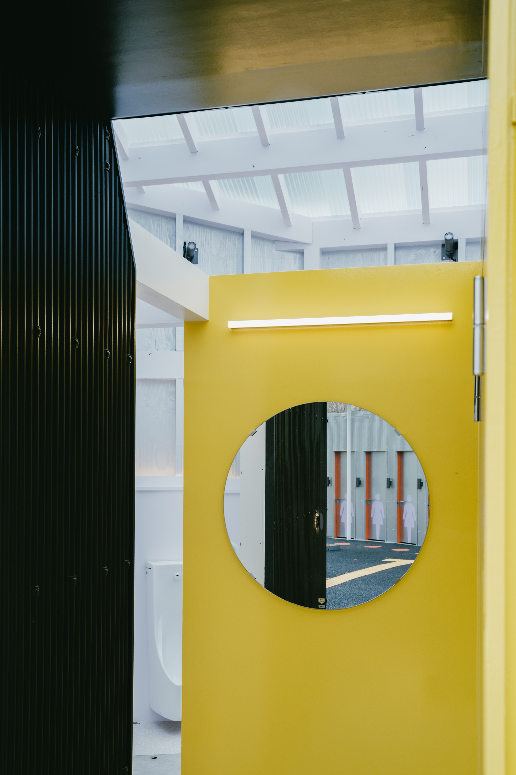 Yellow partition with circular opening revealing interior space under a translucent ribbed ceiling