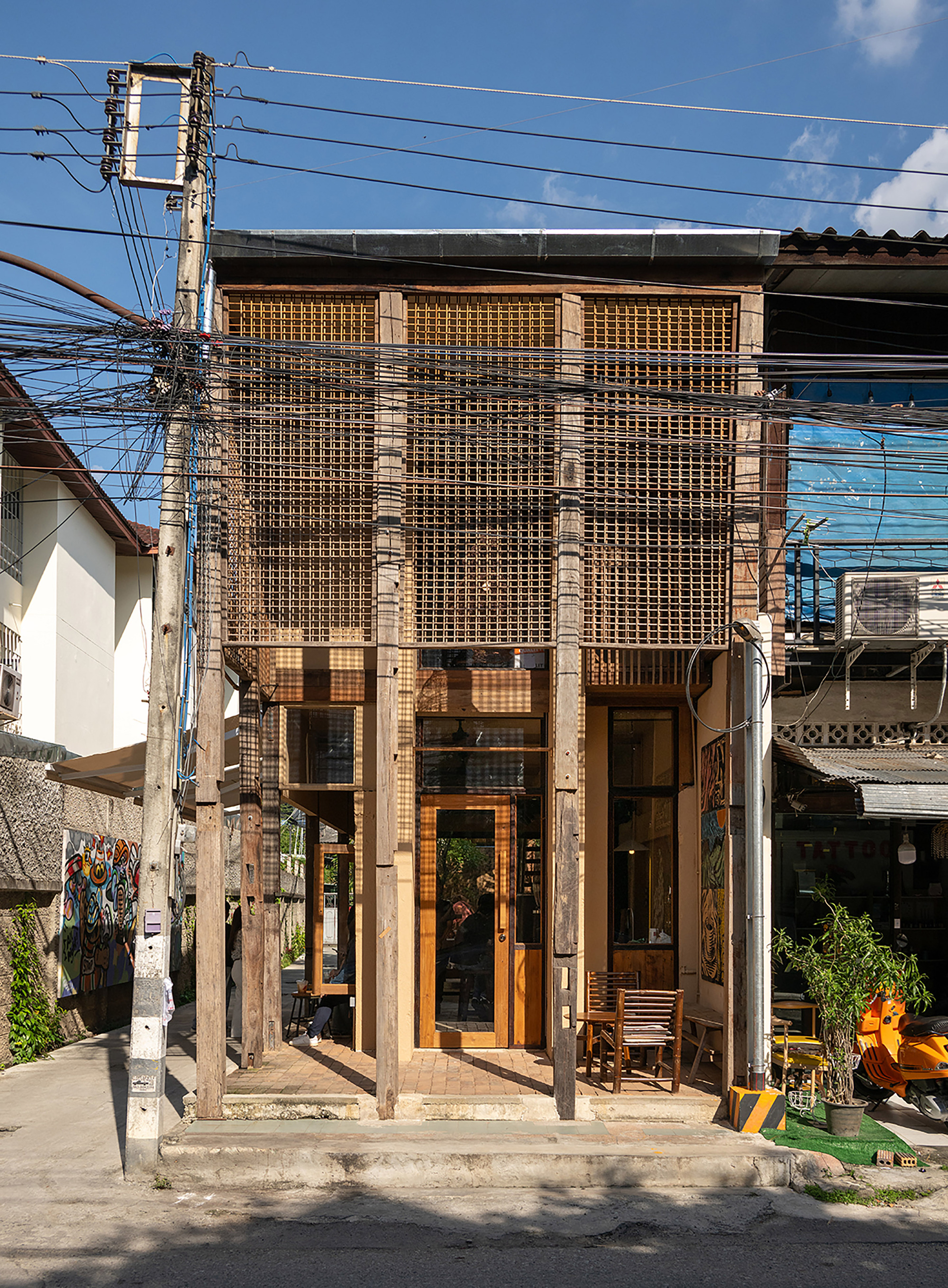 Two-story timber screen facade with brick columns on a residential street beneath overhead power lines
