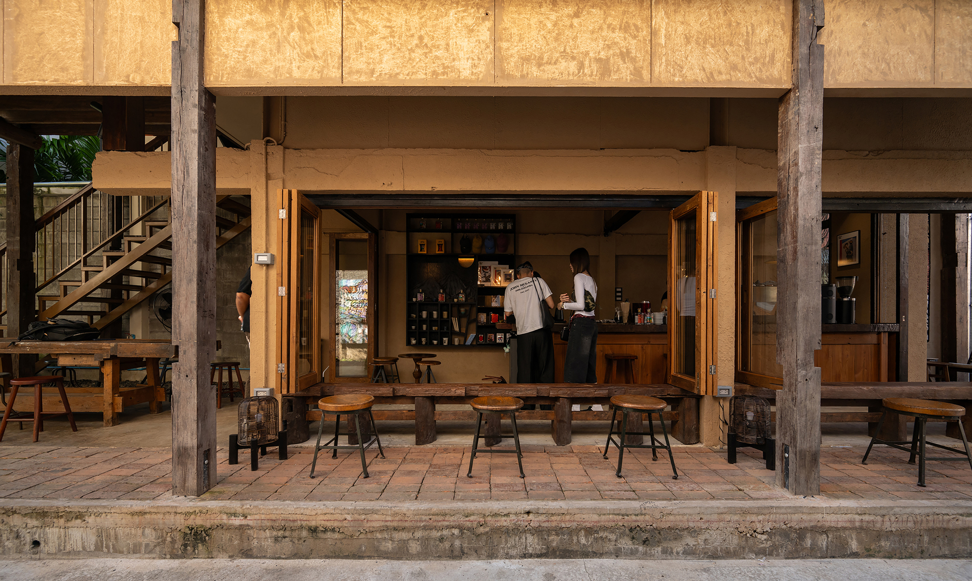 Ground-floor cafe counter with folding timber doors opening to outdoor seating under reclaimed timber beams