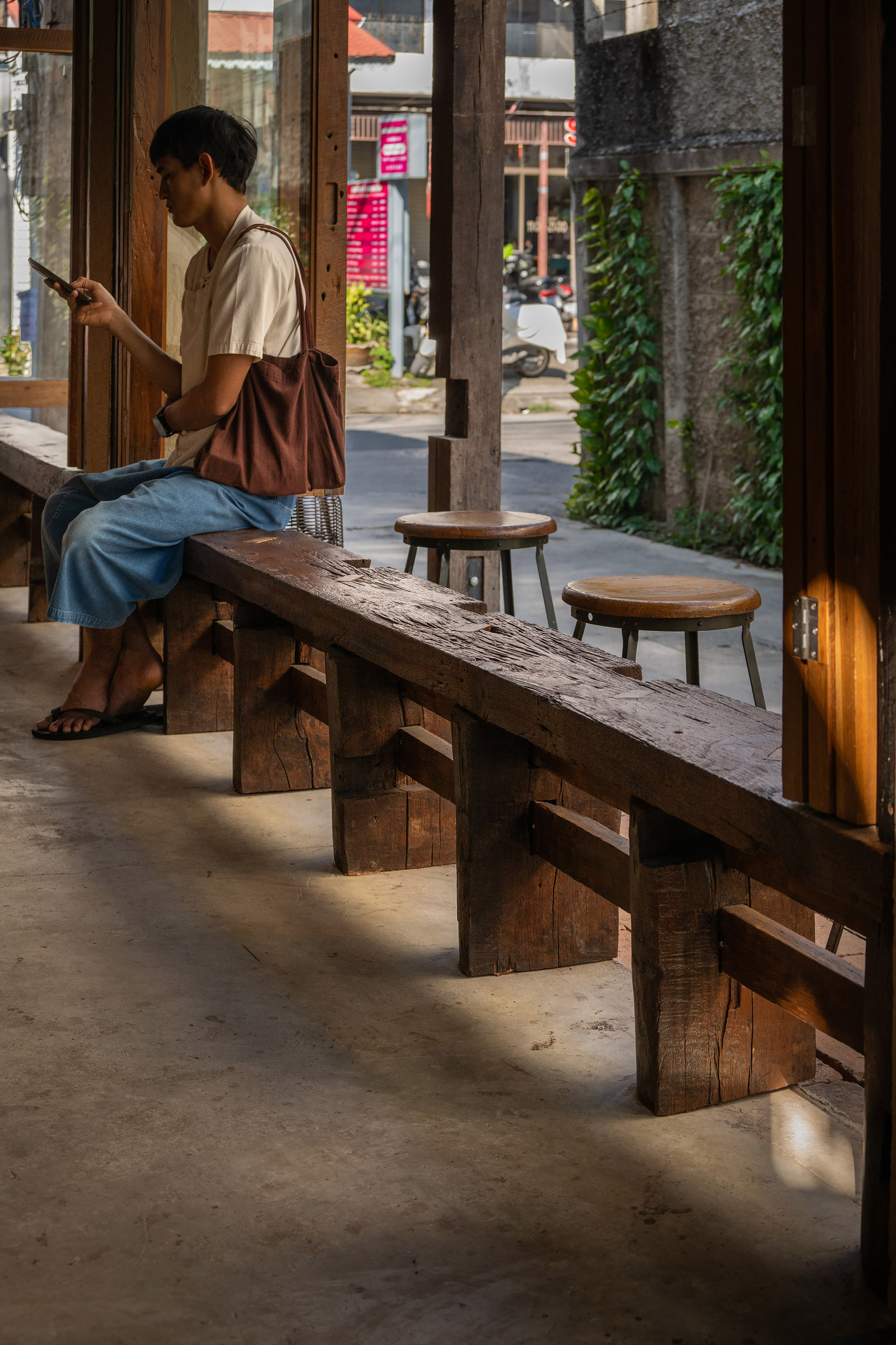 Timber bench and stools along the interior threshold where a person sits reading in natural daylight