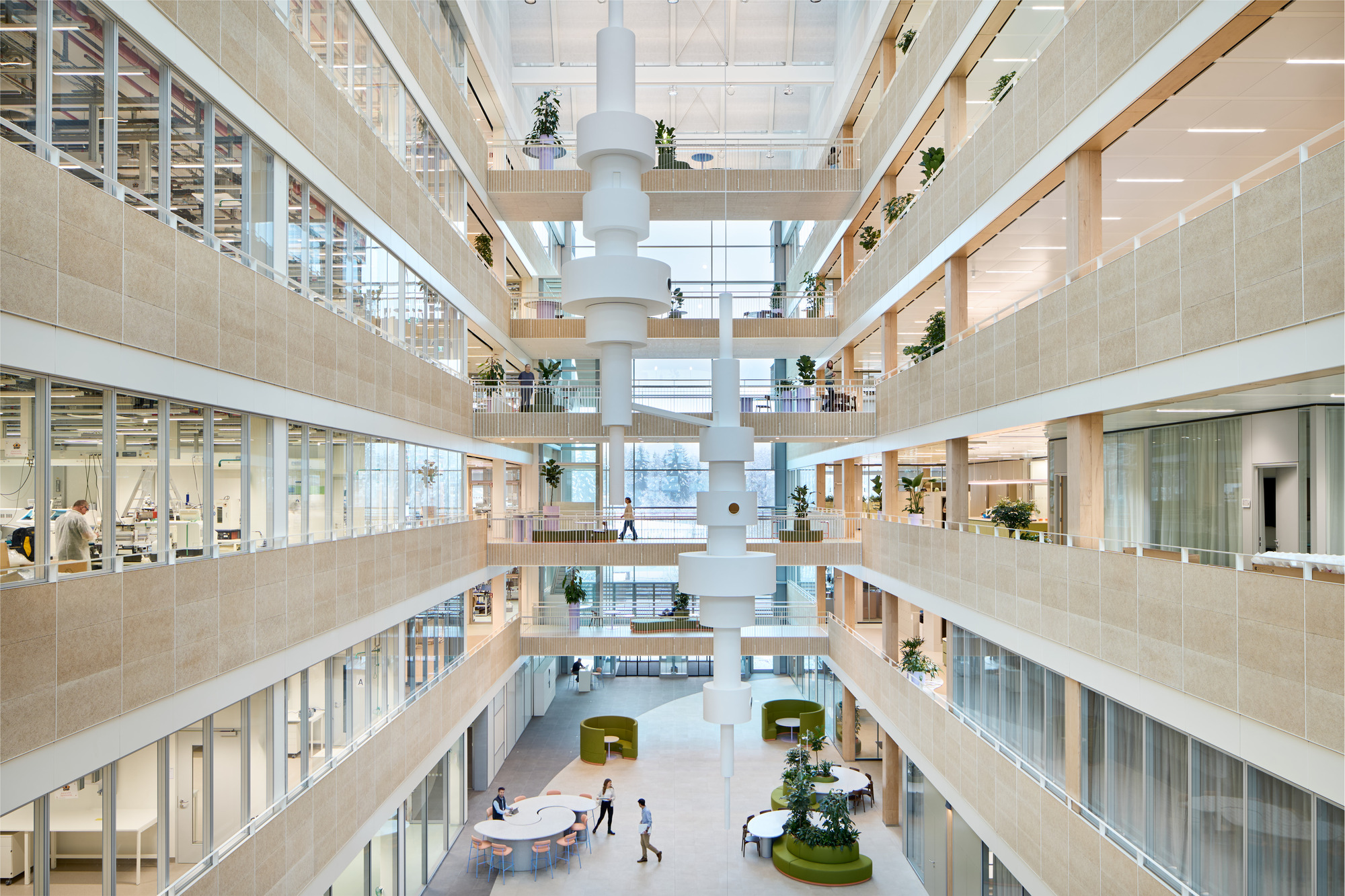 Multi-story atrium with central white column, timber-clad balconies and potted plants on each floor