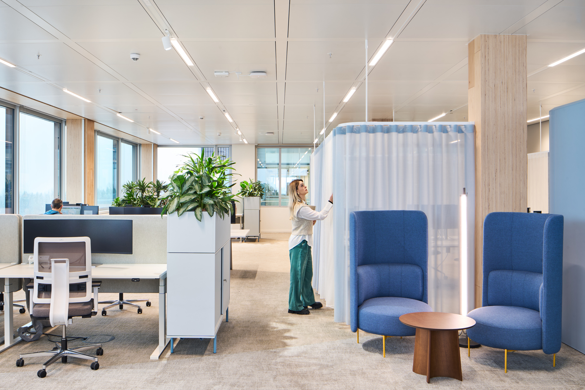 Open office area with blue acoustic booths, workstations and a person standing near curtained seating