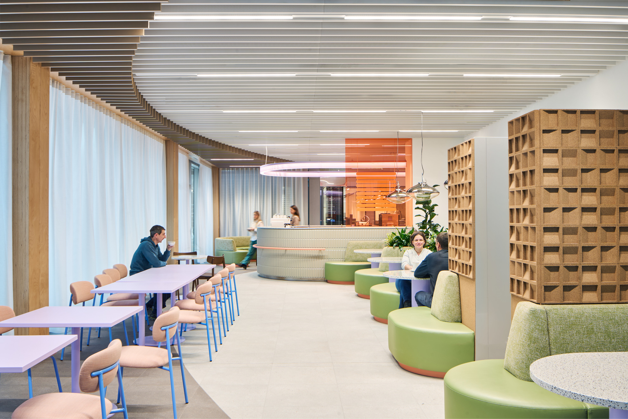 Staff lounge with curved timber-battened wall, green modular seating and people working at tables