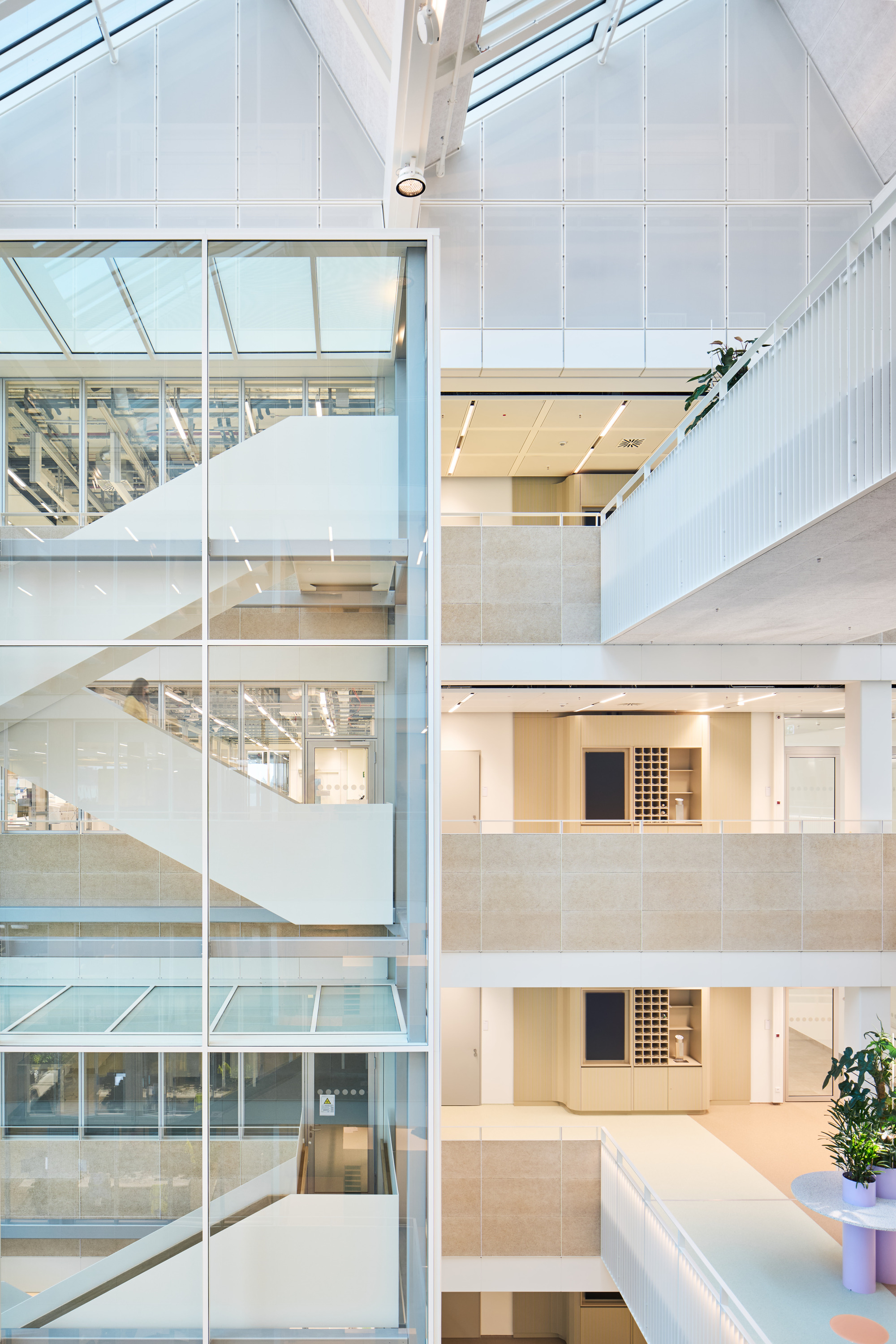 Glazed facade revealing stacked office levels with pale timber ceilings and white staircases