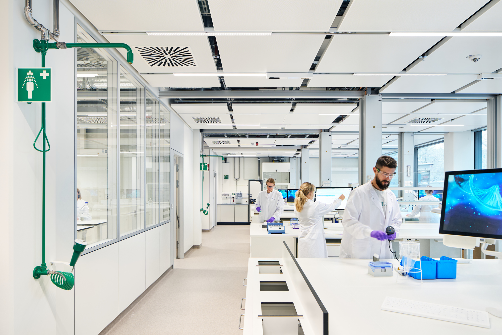 Laboratory interior with white benches, exposed services ceiling and researchers in coats