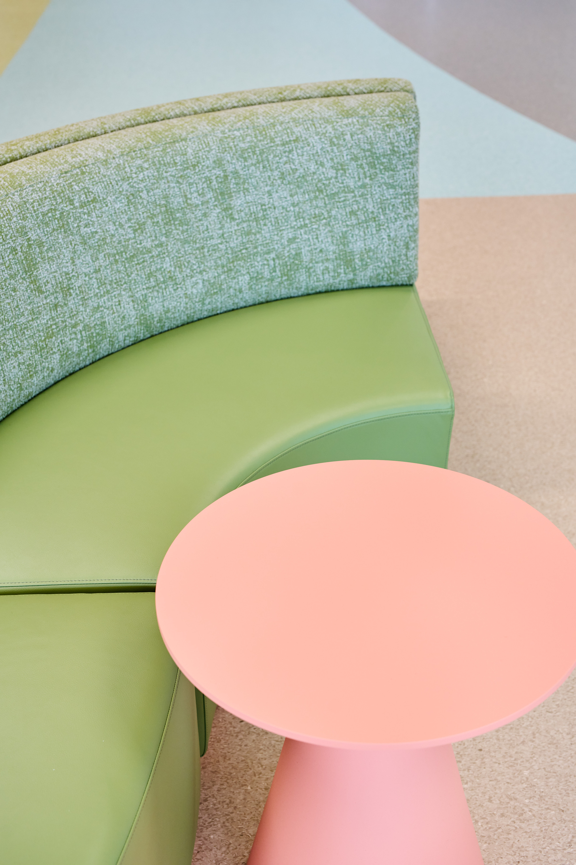 Close-up of pastel pink side table beside green upholstered banquette on terrazzo flooring