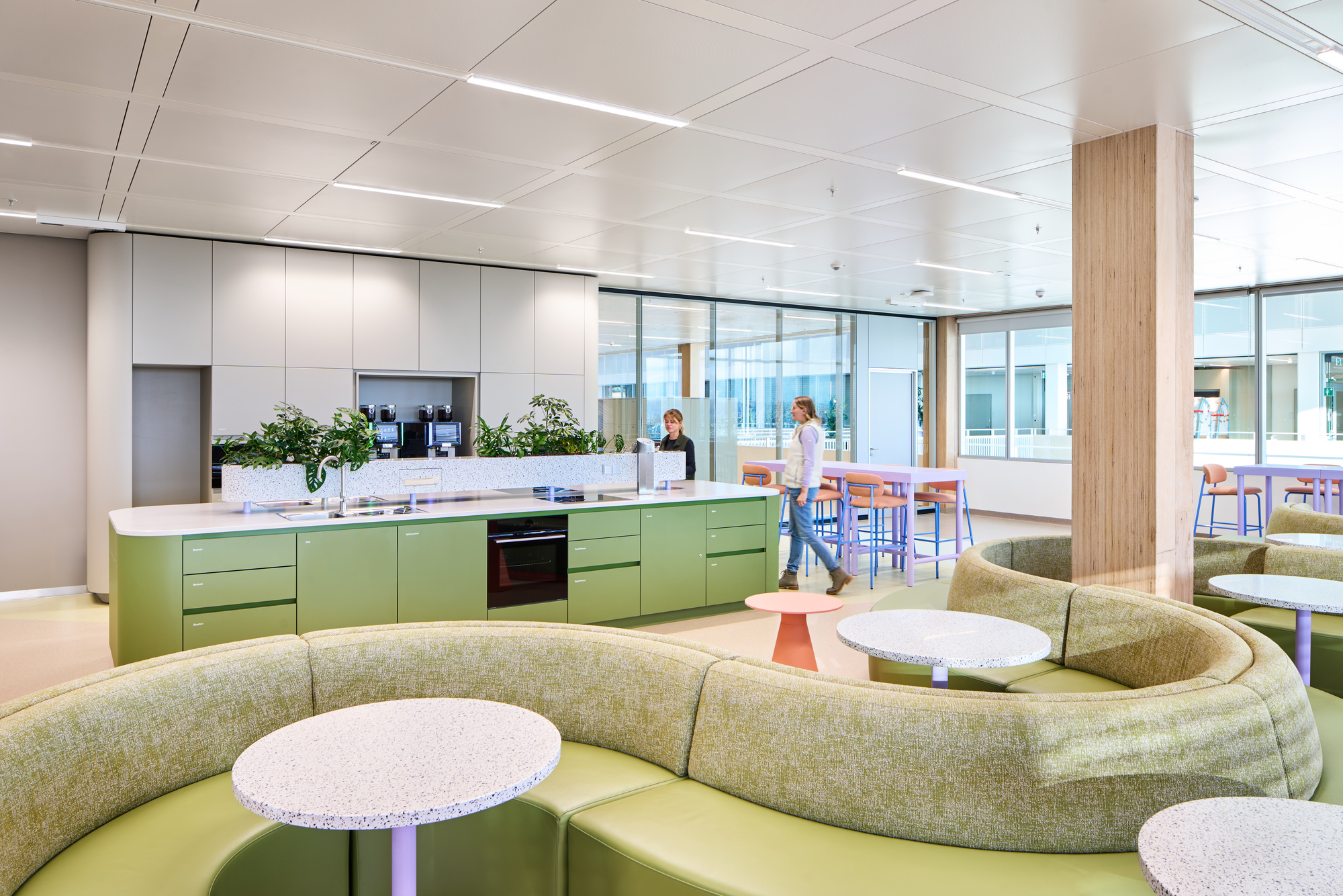 Breakroom with long green kitchen island, white cabinetry and curved lounge seating under recessed lighting