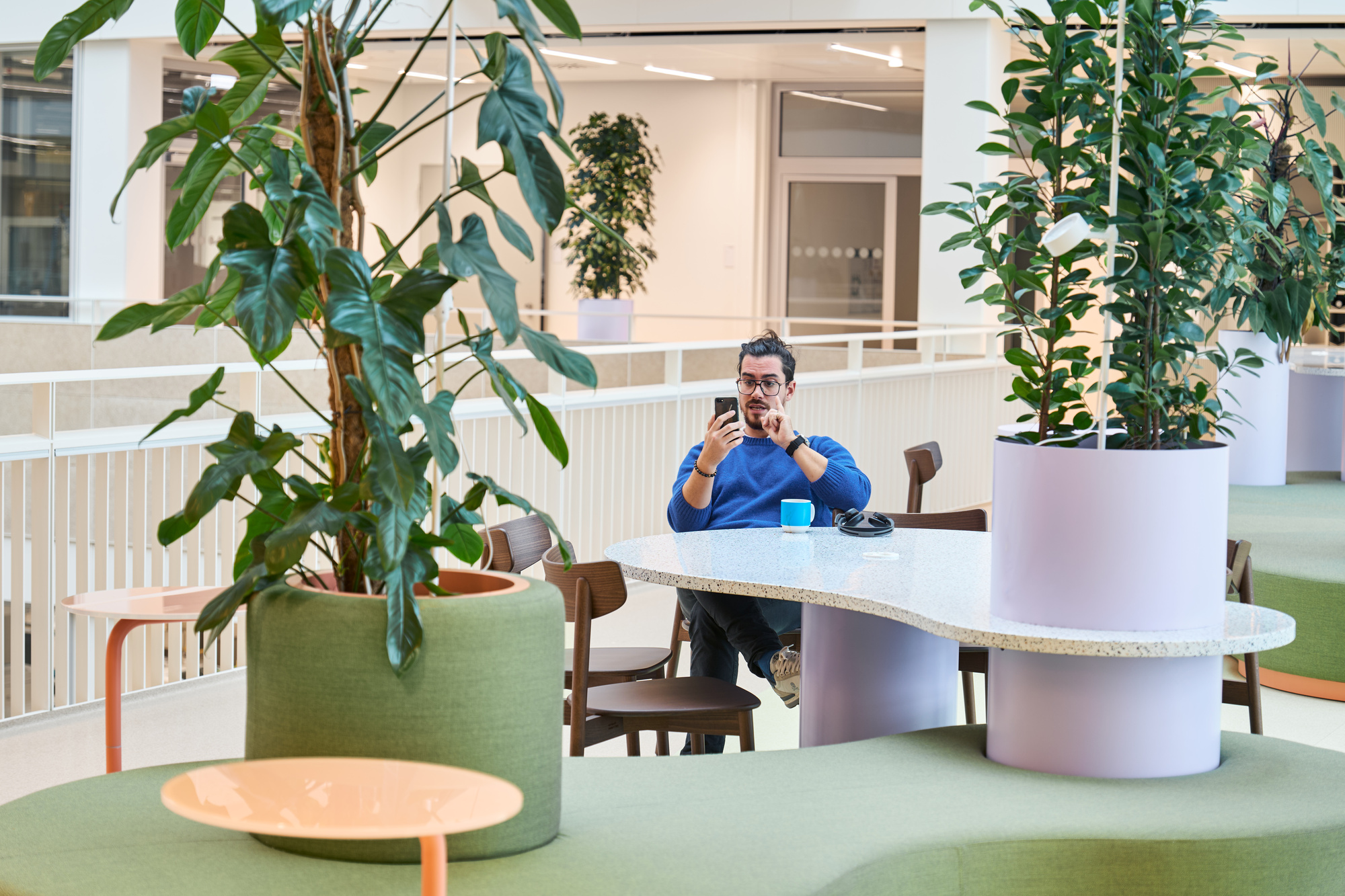 Open workspace with curved banquettes, cylindrical planters and a person seated at a terrazzo-topped table