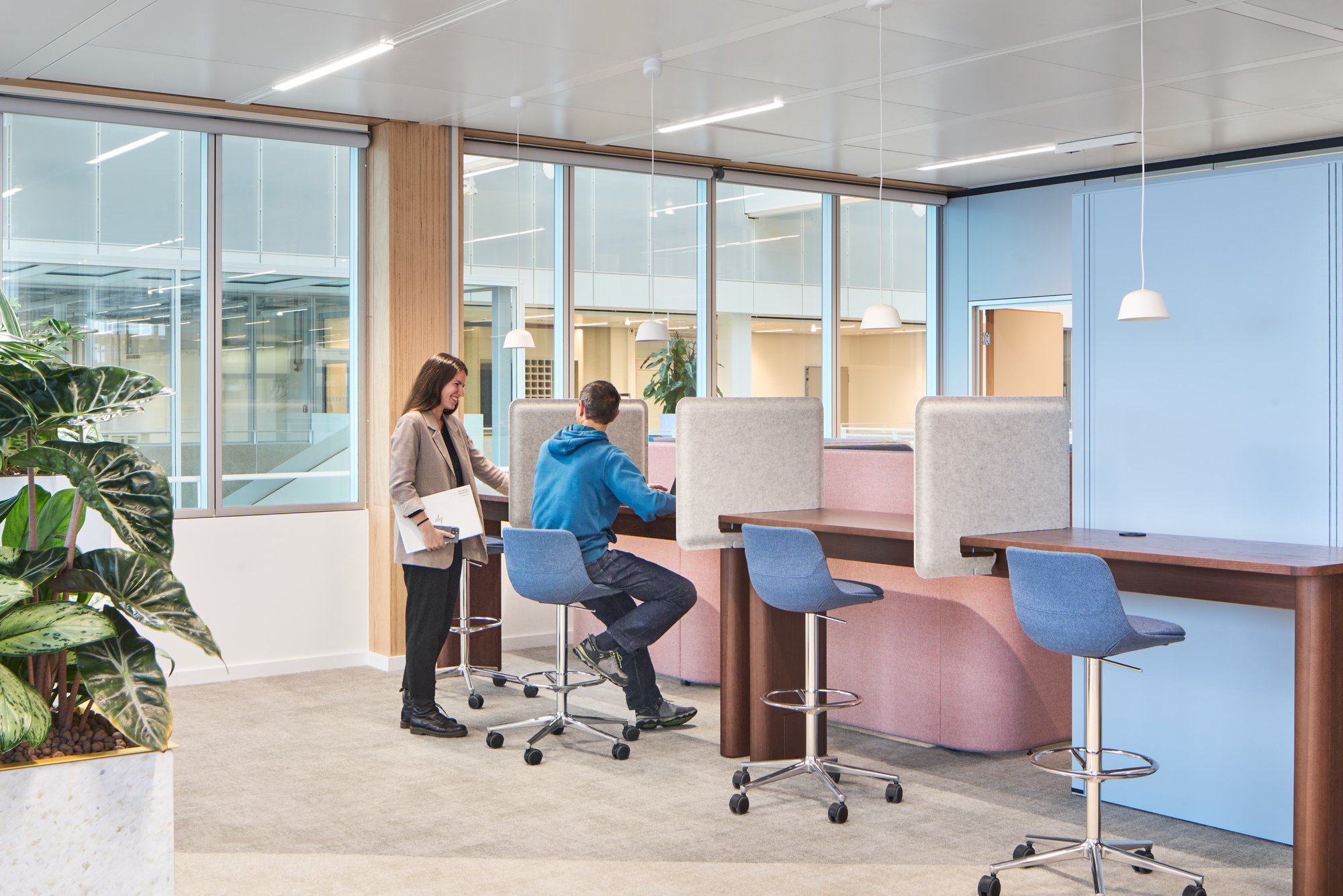 High-top collaboration area with blue stools and fabric privacy screens beside a glass-walled conference room