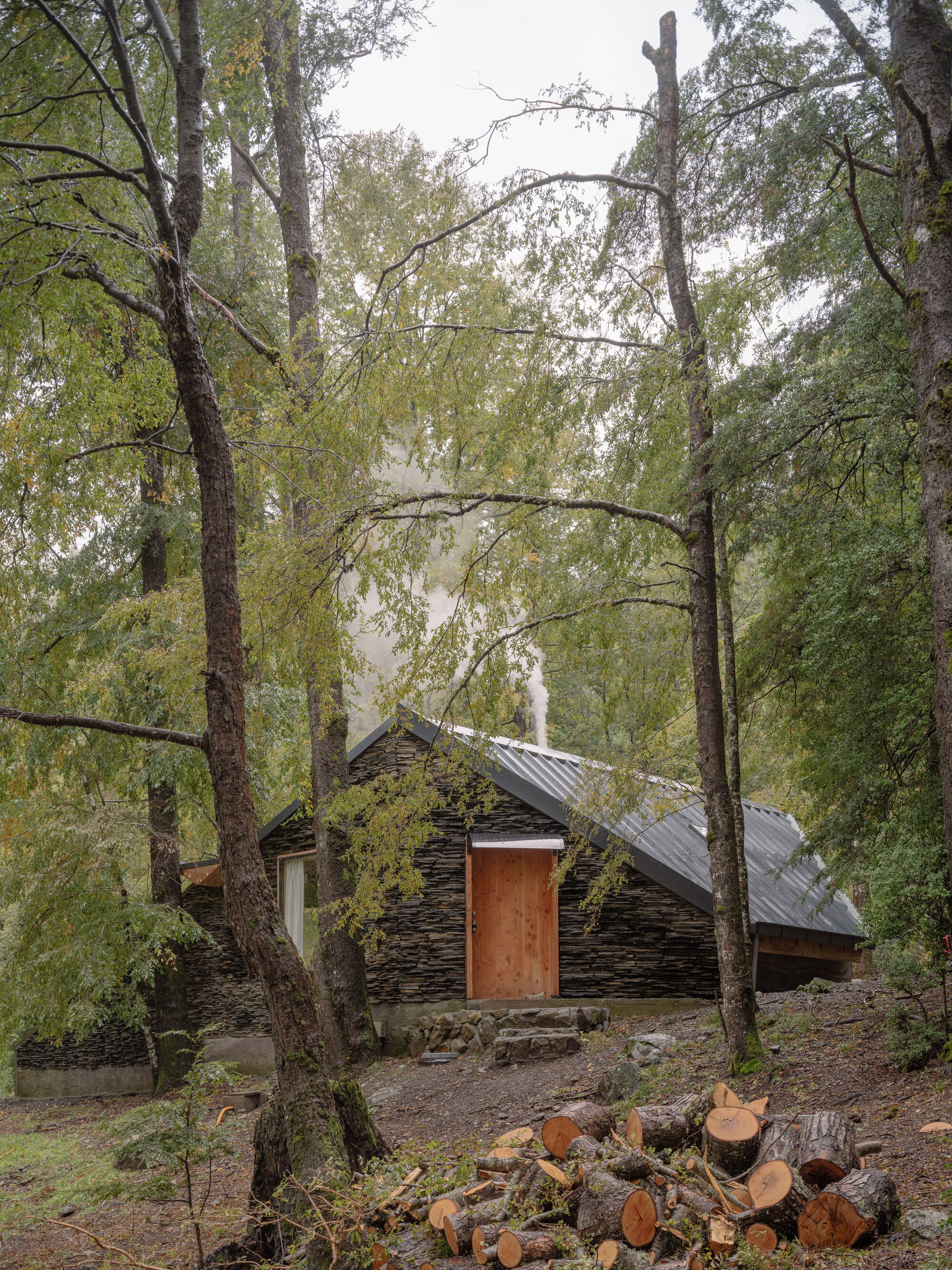 Side view of the peaked stone roof with timber door and stacked firewood in the foreground