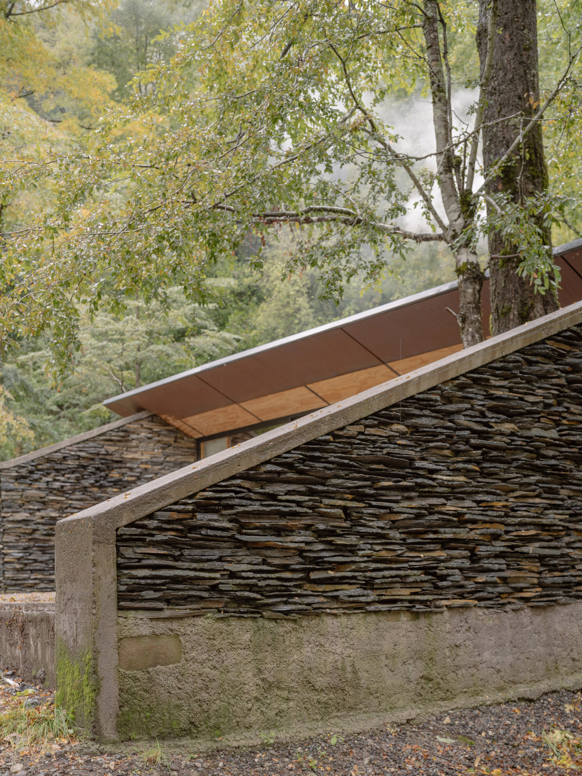 Detail of cantilevered roof with timber soffit and concrete edge above dry-stacked slate wall