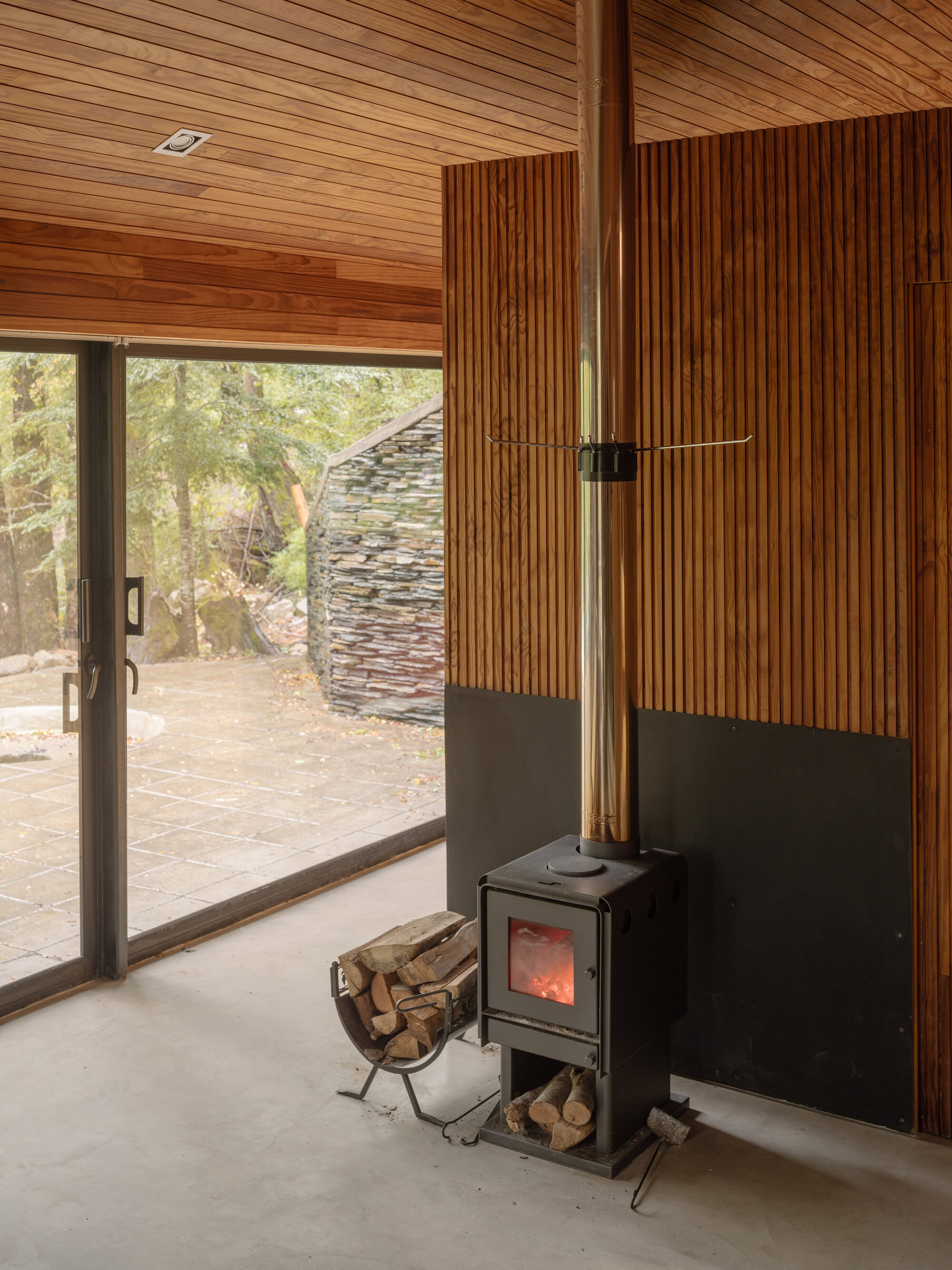 Interior with wood stove on black steel backing against vertical timber slat wall and ceiling