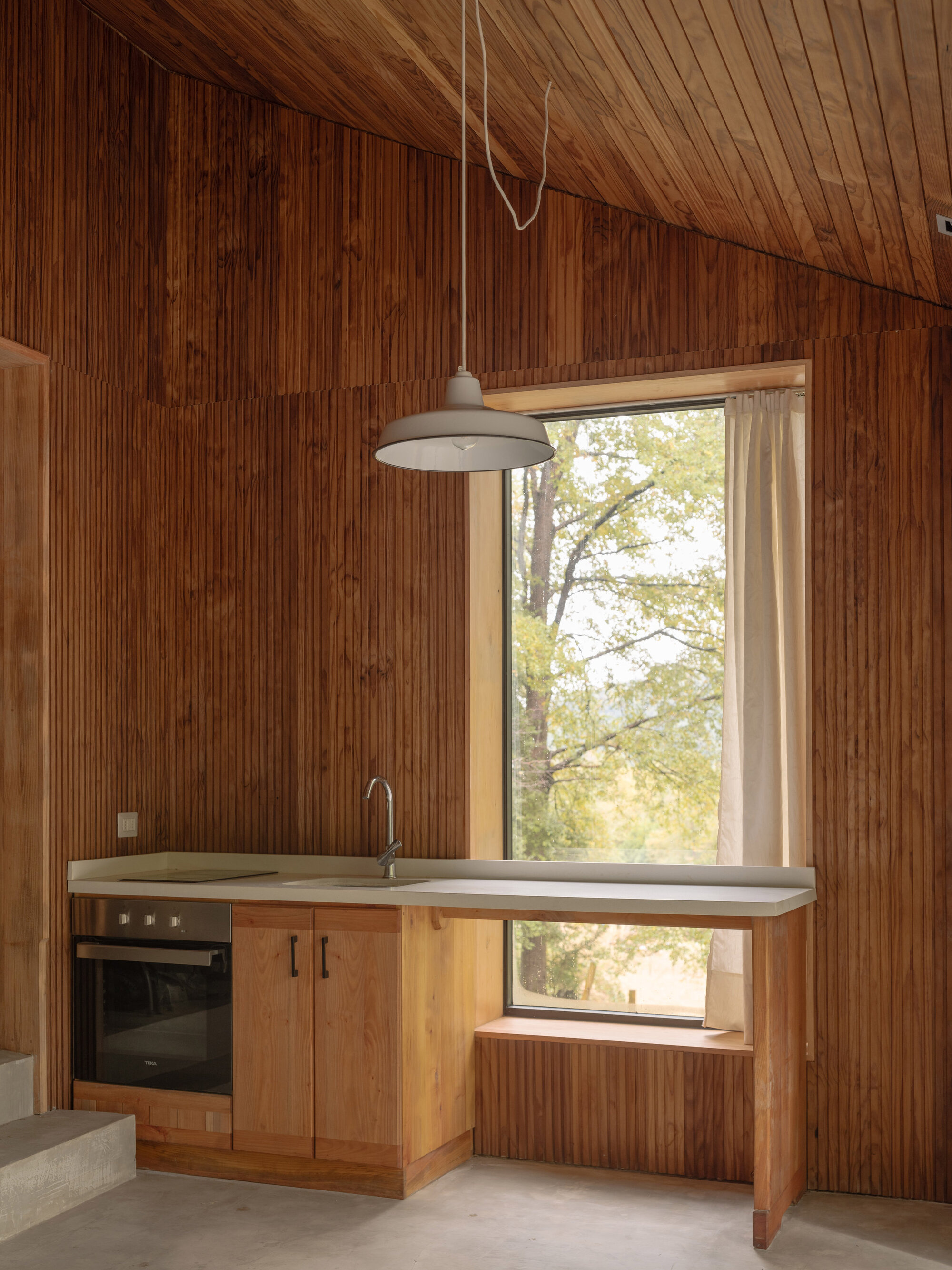 Kitchen with pale countertop and oven under pendant light framed by vertical timber paneling