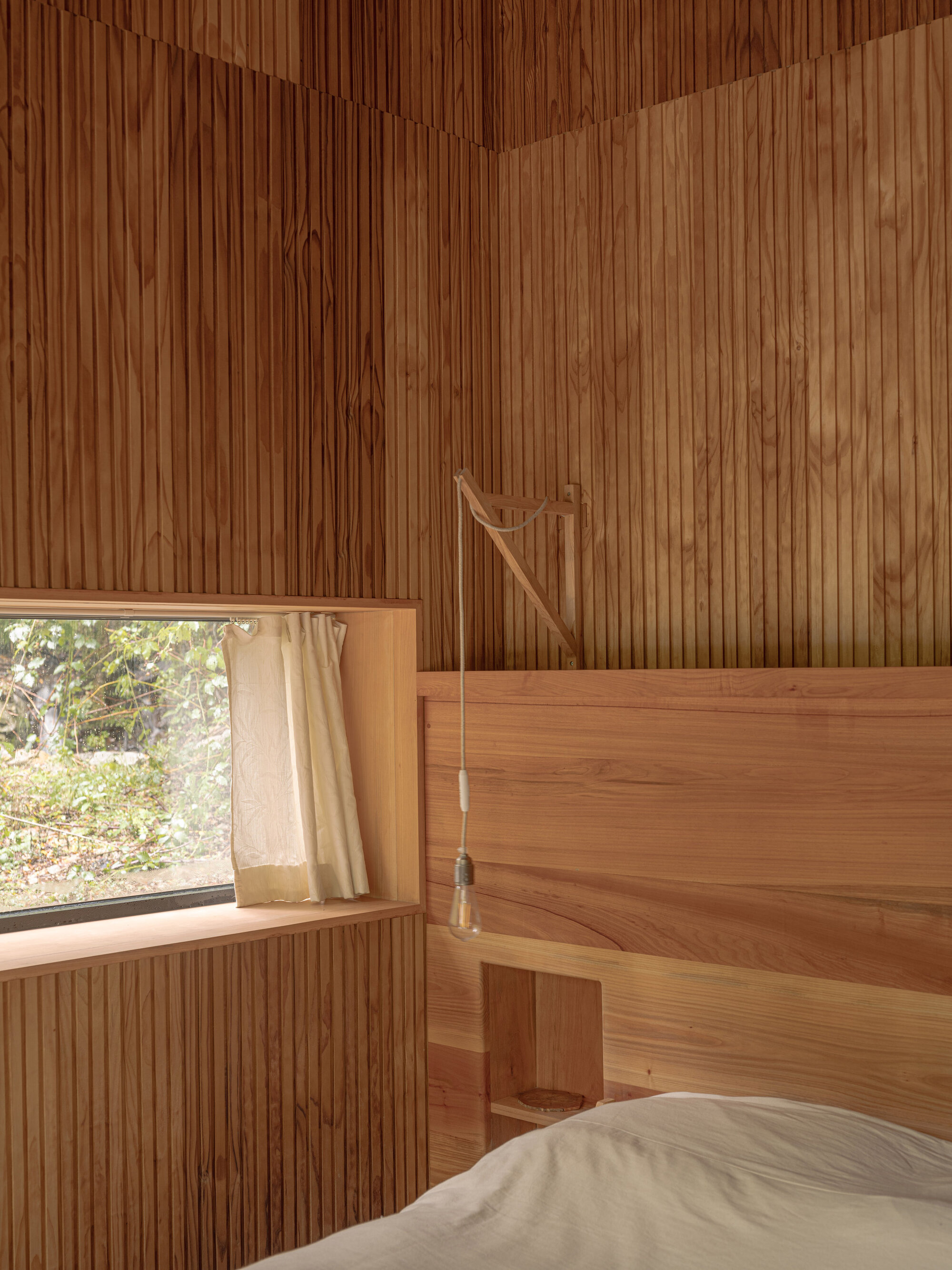 Bedroom with vertical timber slat walls and ceiling, a wood-framed bed and a window framing foliage outside