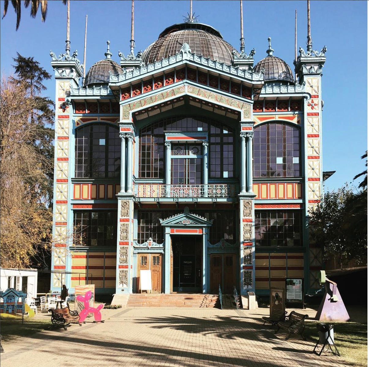 Front facade with ornate domed towers, arched windows and striped detailing under a clear blue sky