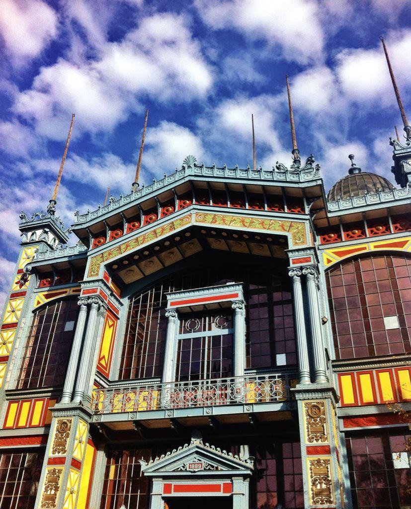 Upper facade detail showing central balcony, glazed columns and decorative banding beneath scattered clouds