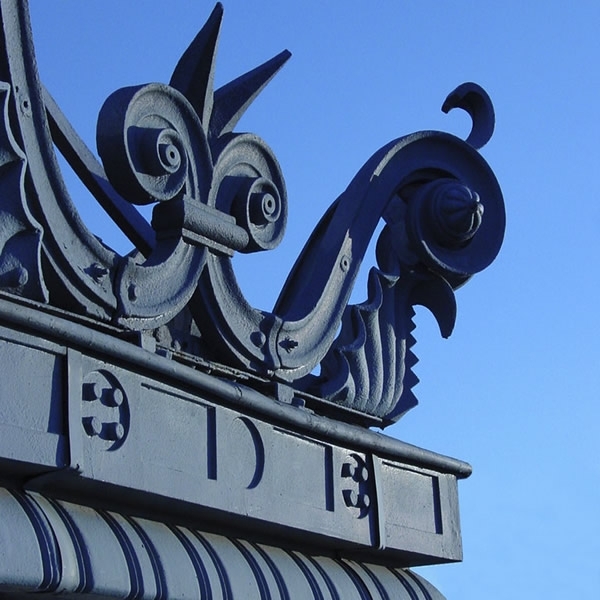 Close-up of the wrought iron rooftop ornamentation with scrollwork and spikes against a clear blue sky
