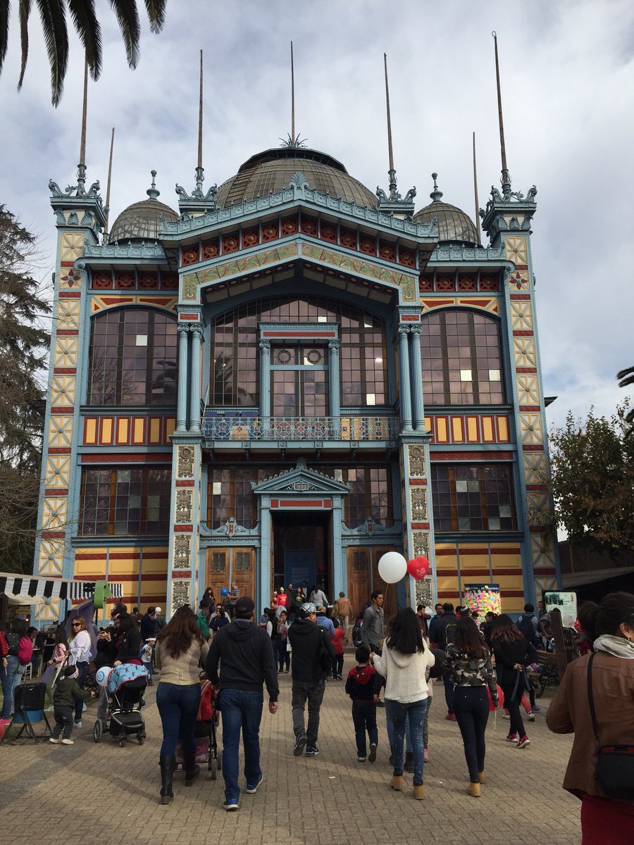 Facade with domed roof, ornate metalwork balconies, and tiled surfaces as visitors gather at the entrance