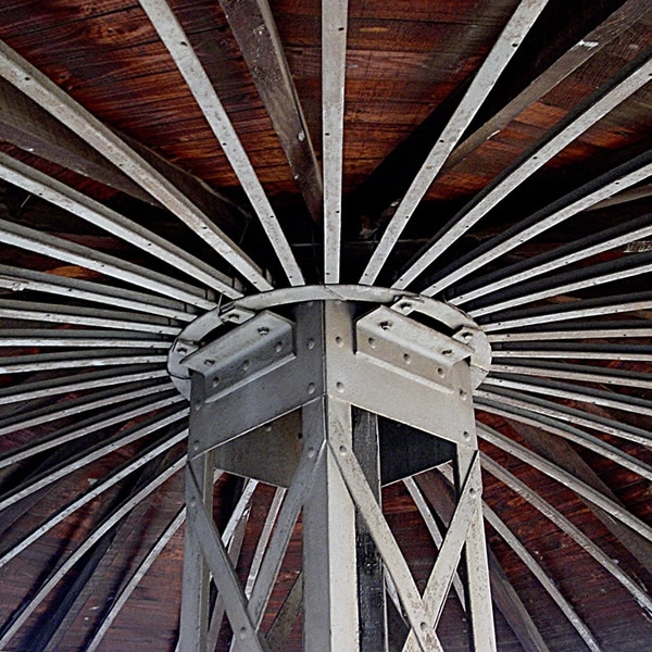 Looking up at the radiating steel beams converging at a central column node beneath timber decking