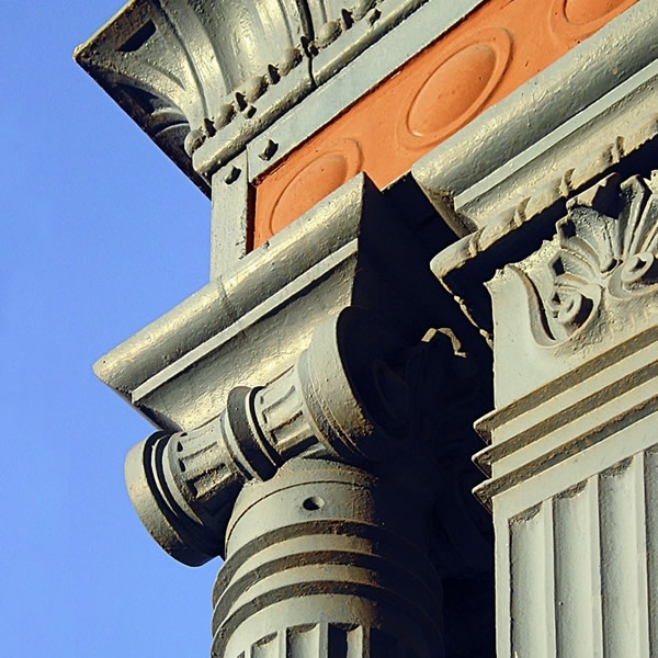 Detail of a fluted column capital with terracotta medallion and carved foliate ornament in afternoon light